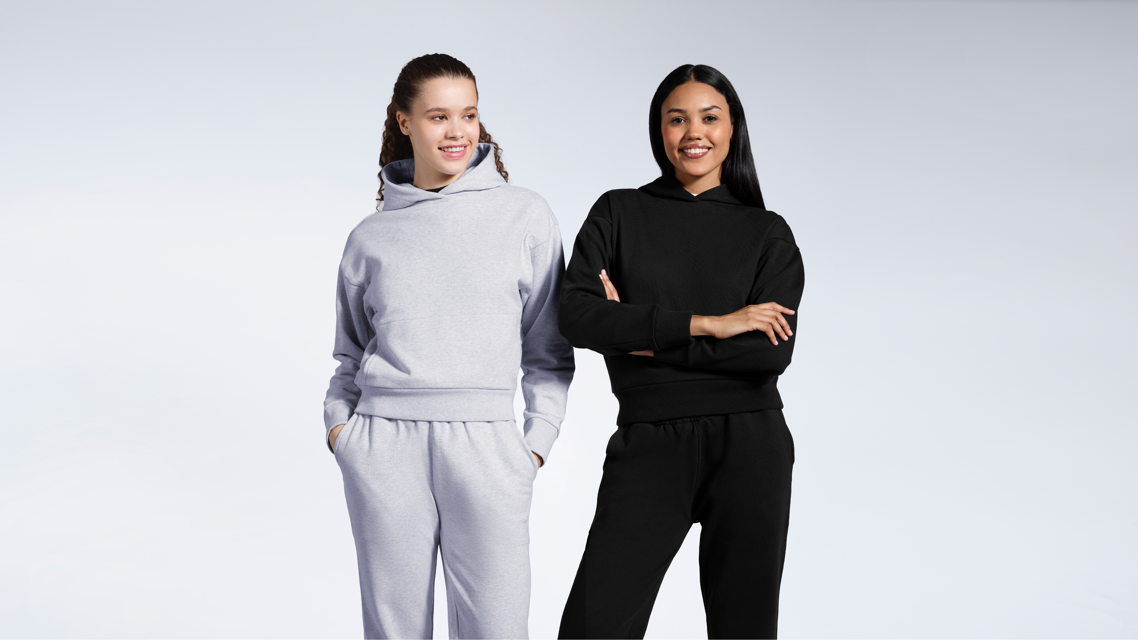 Two women smiling, modelling plain matching black and grey heavyweight organic cotton tracksuits.