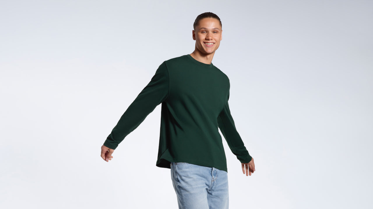 A man walking and smiling, modelling a plain green long sleeve organic cotton t shirt.