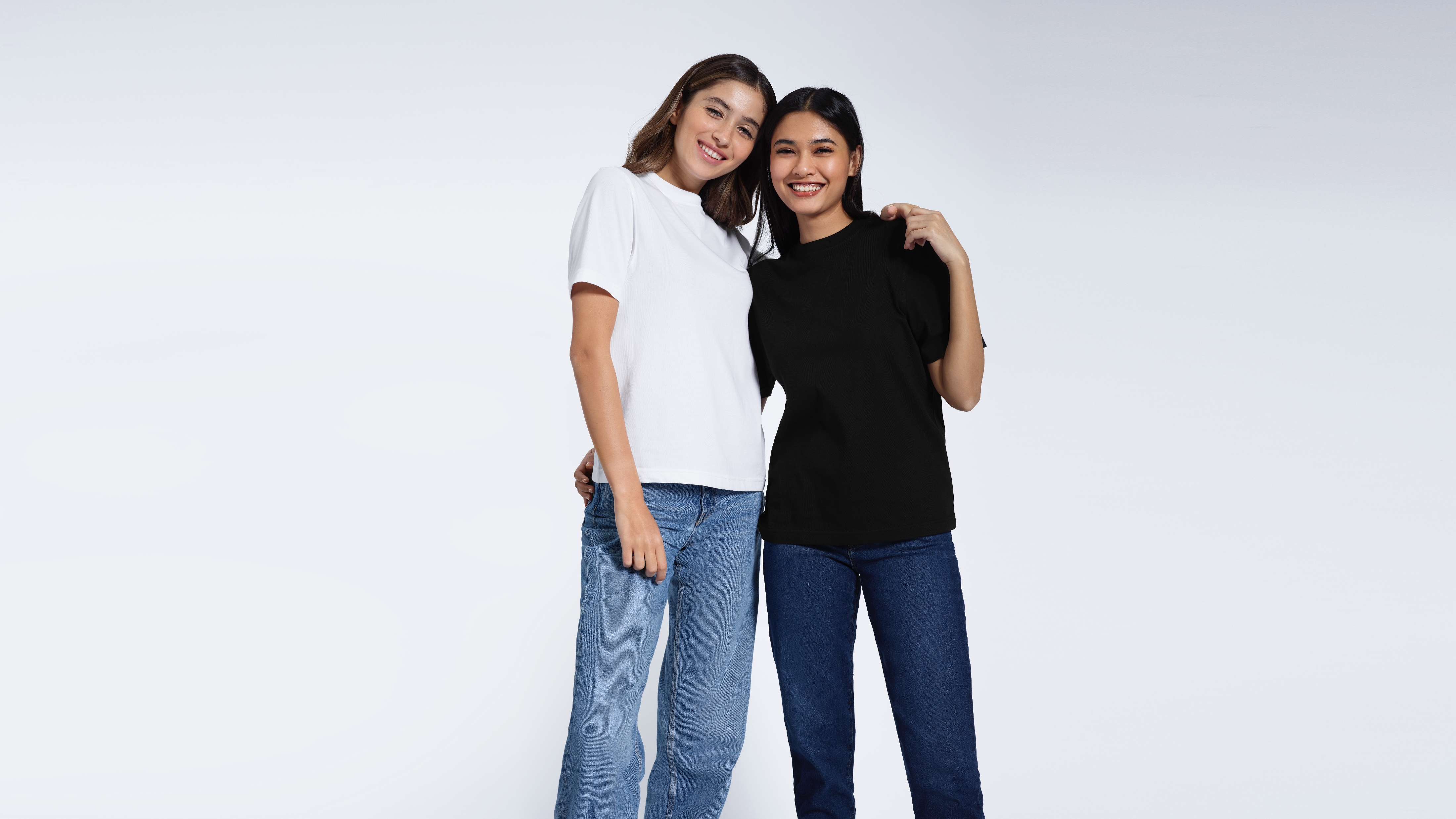 Two women with their arms round eachother smiling, modelling plain black and white organic cotton t shirts.
