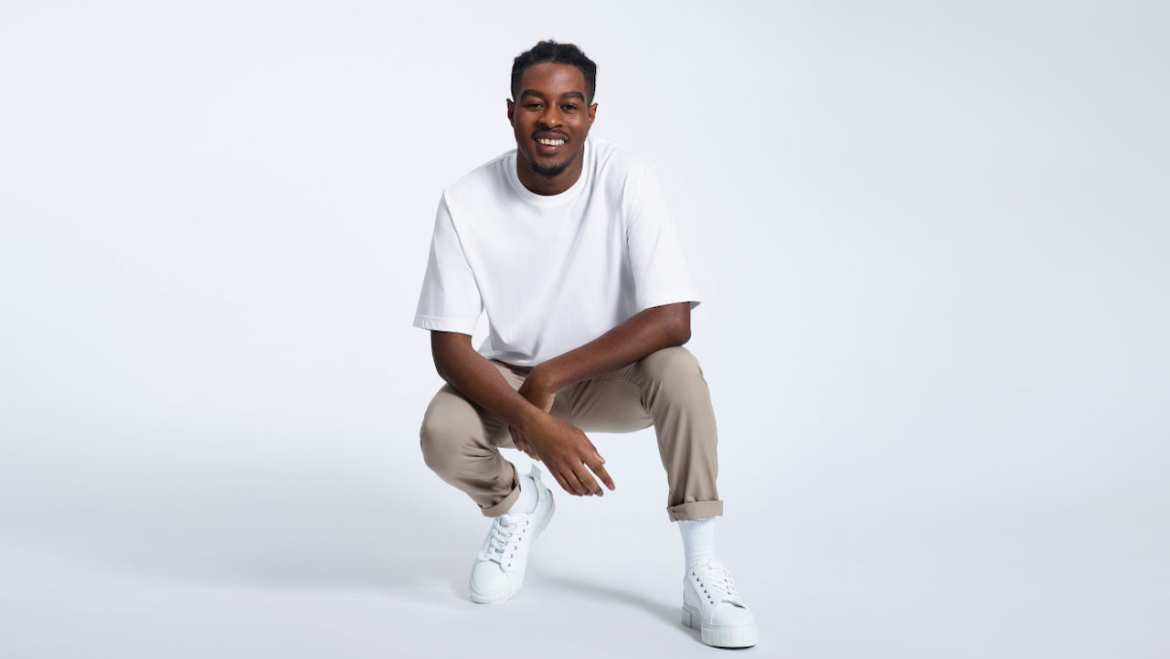 A man kneeling down smiling, modelling a plain white oversized heavyweight organic cotton t shirt.
