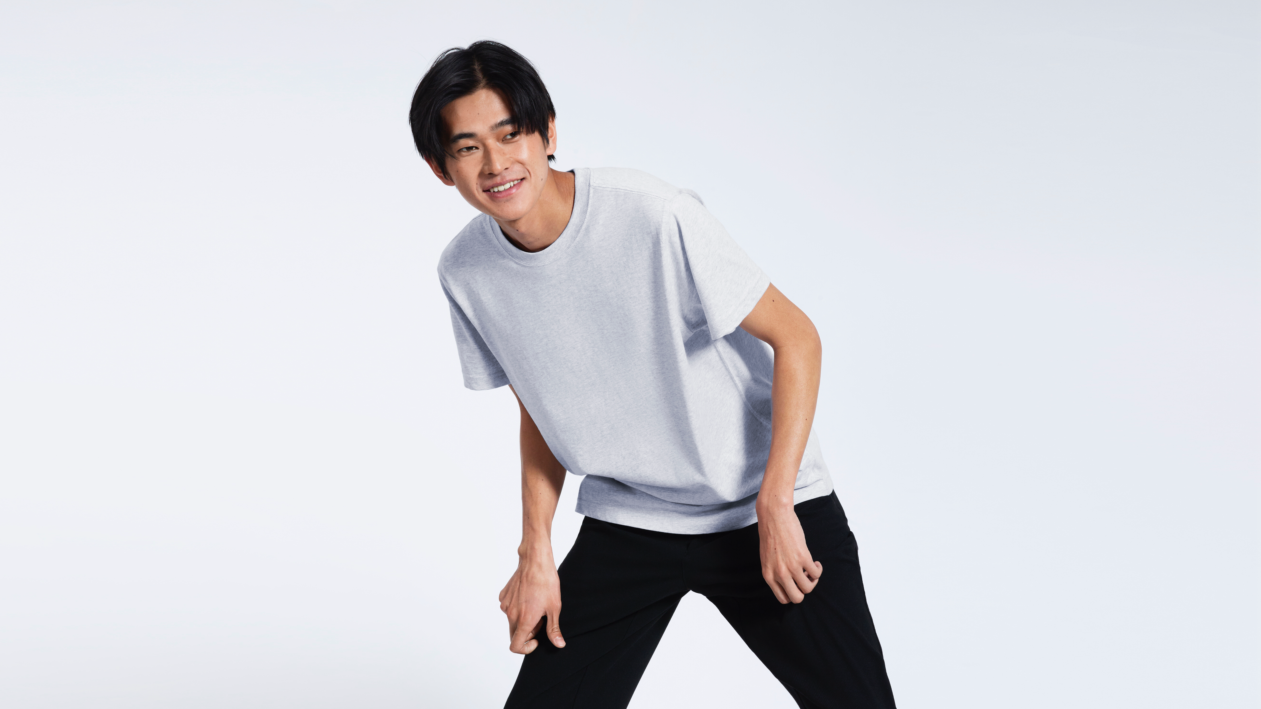 A man smiling bending over slightly, modelling a plain grey organic cotton t shirt.