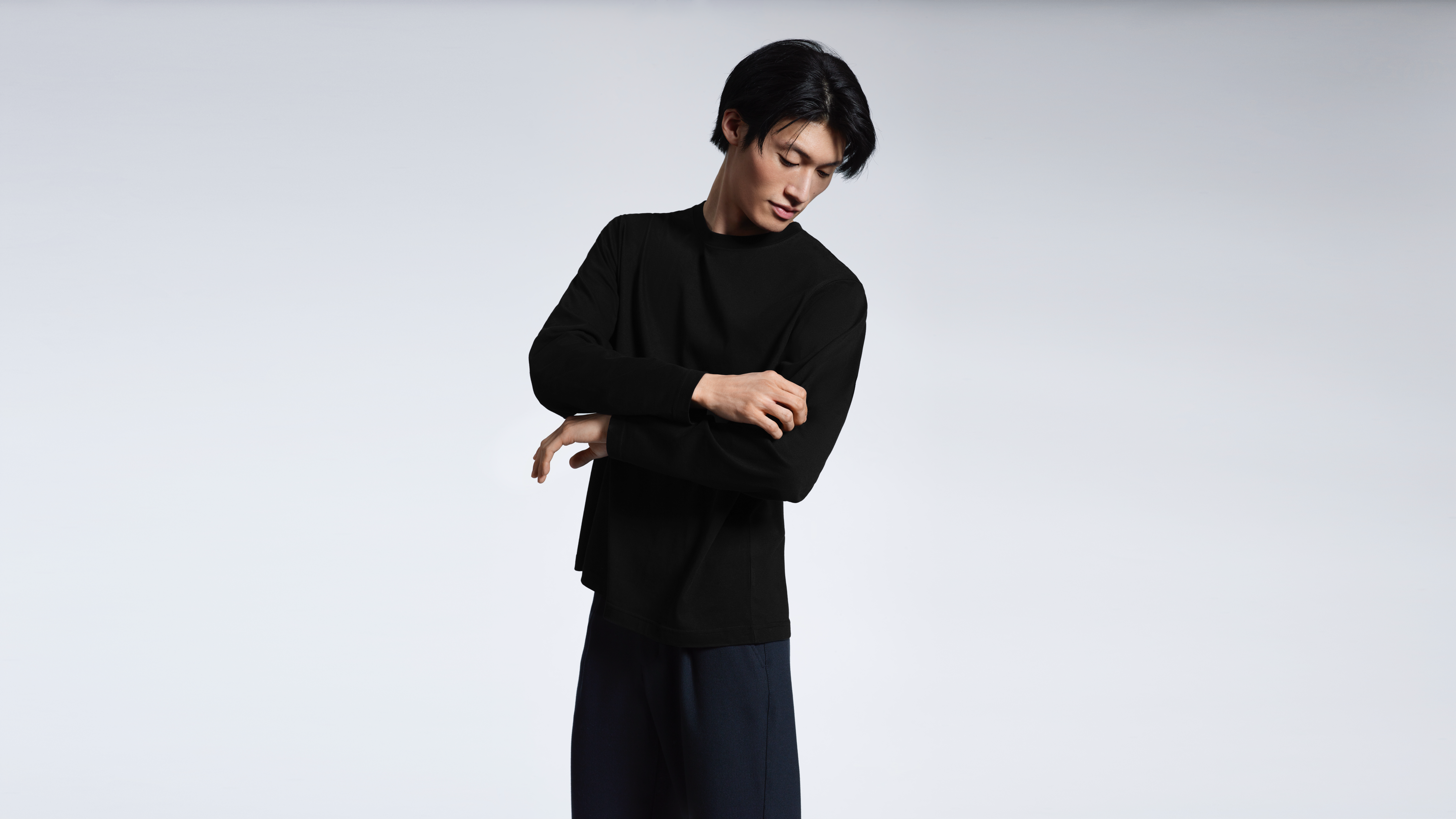 A man looking down and touching his sleeve, modelling a plain black long sleeve organic cotton t shirt.