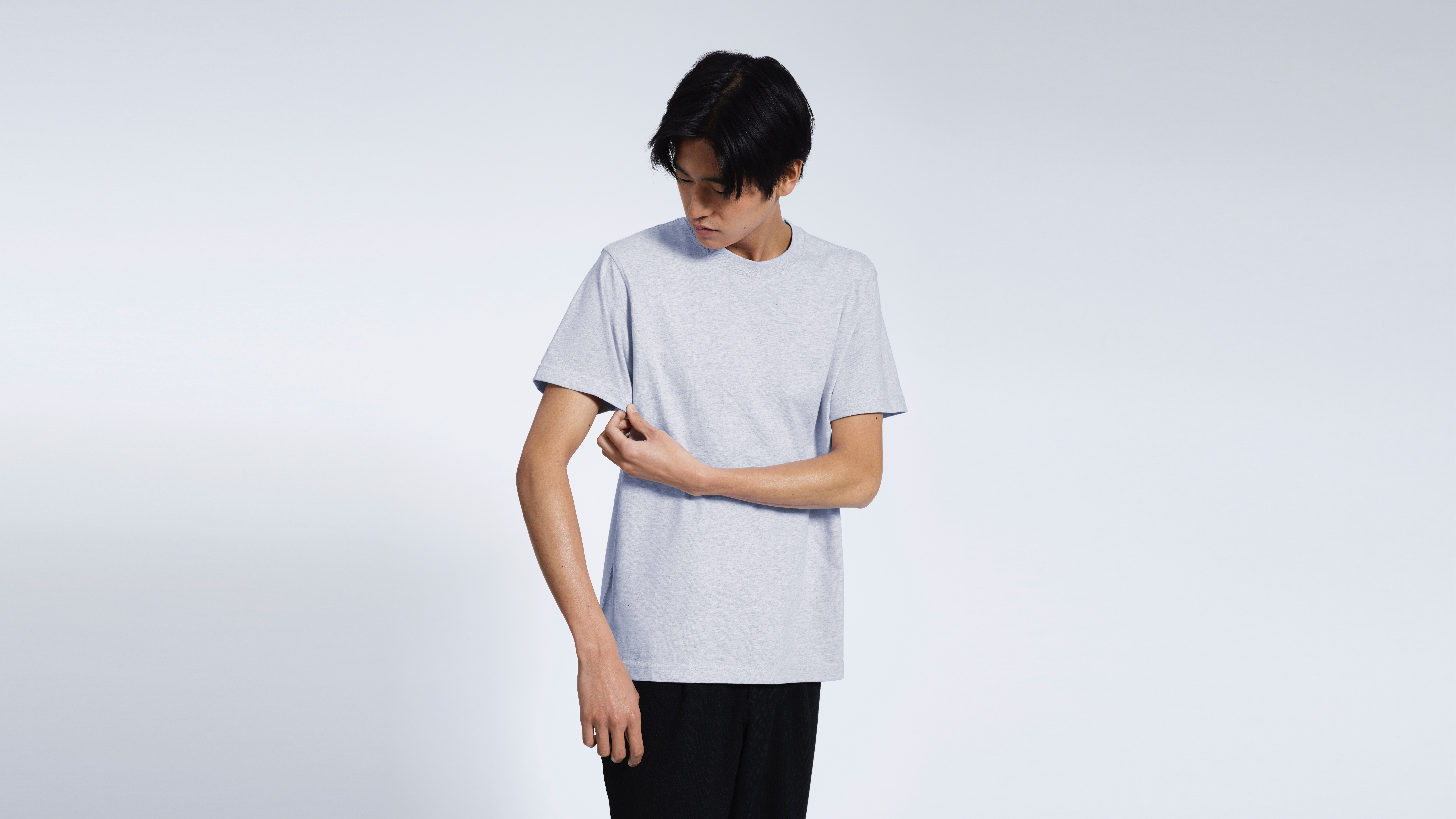 A man looking down touching his sleeve, modelling a plain grey short sleeve organic cotton t shirt.