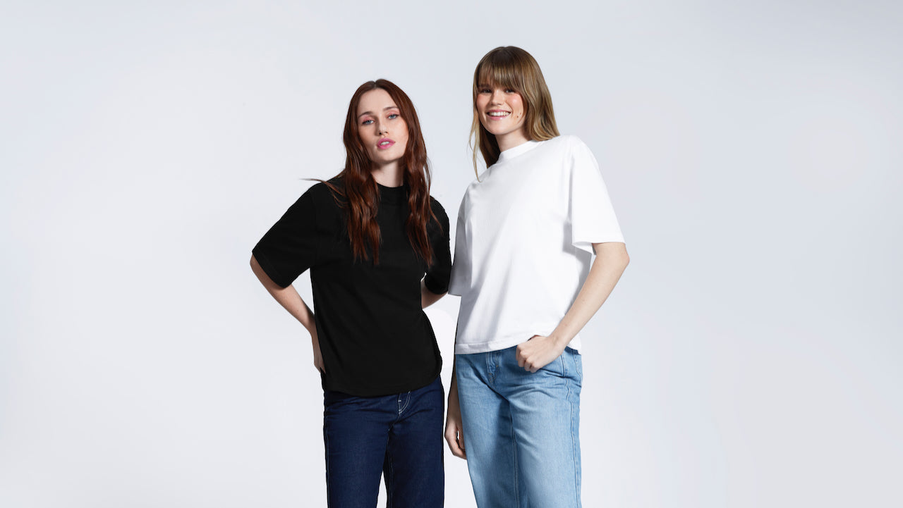 Two women looking at the camera, modelling heavyweight organic cotton boxy, oversized plain white and black short sleeve t shirts.