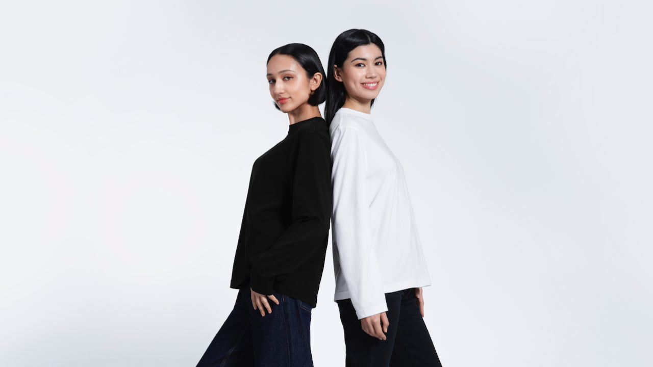 Two women back to back smiling into the camera, modelling plain black and white organic cotton long sleeve t shirts.