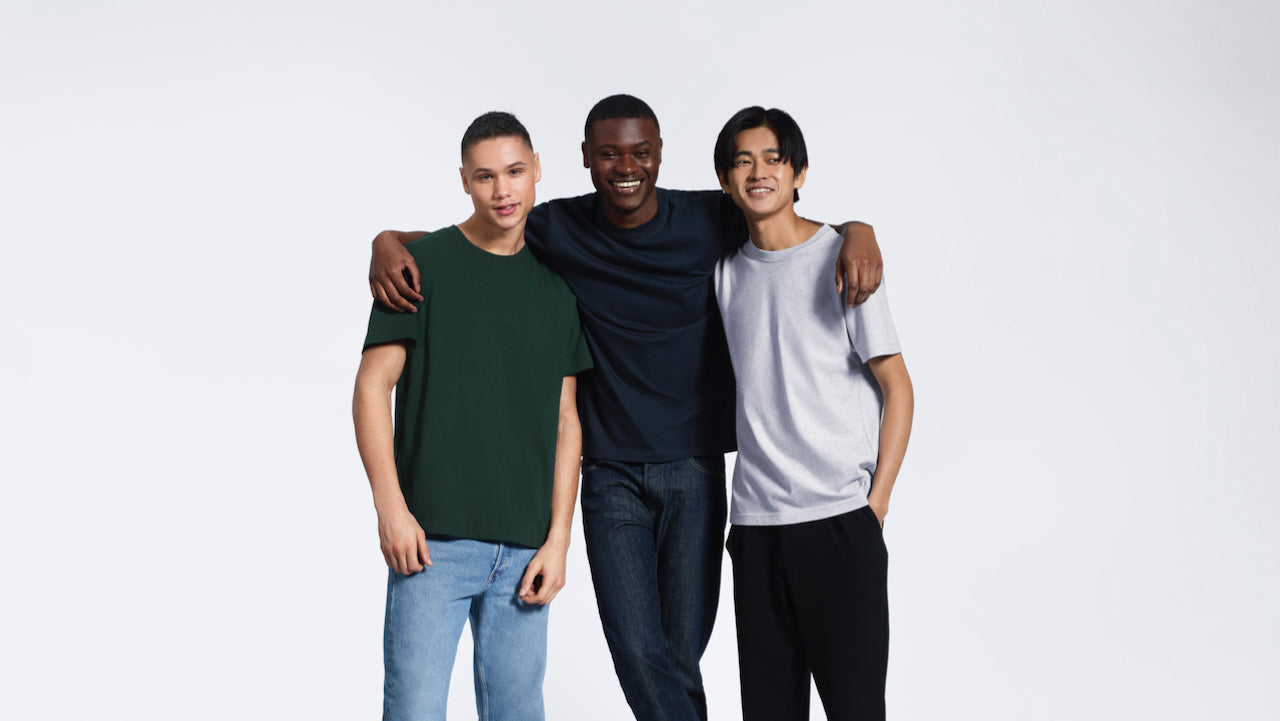 Three men smiling with their arms round eachother, modelling plain green, navy and grey organic cotton t shirts.