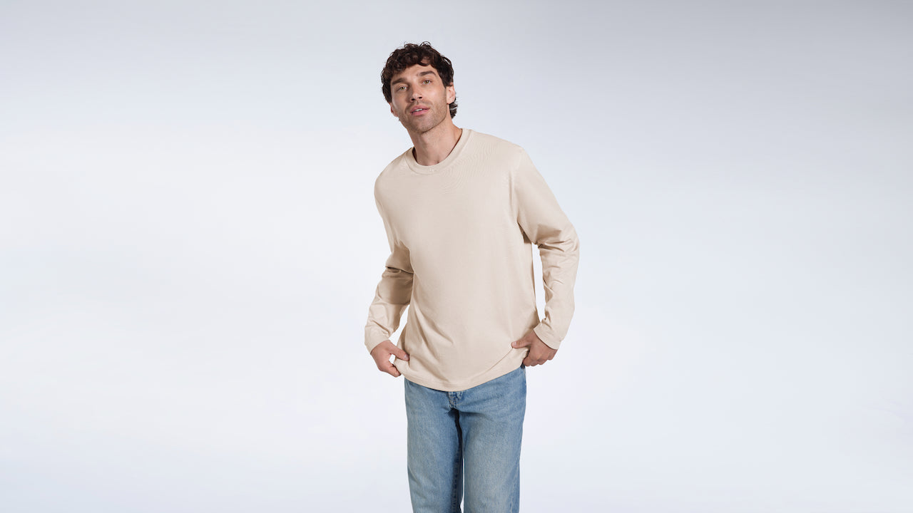 A man looking into the camera, modelling a stone coloured long sleeve, organic cotton t shirt.
