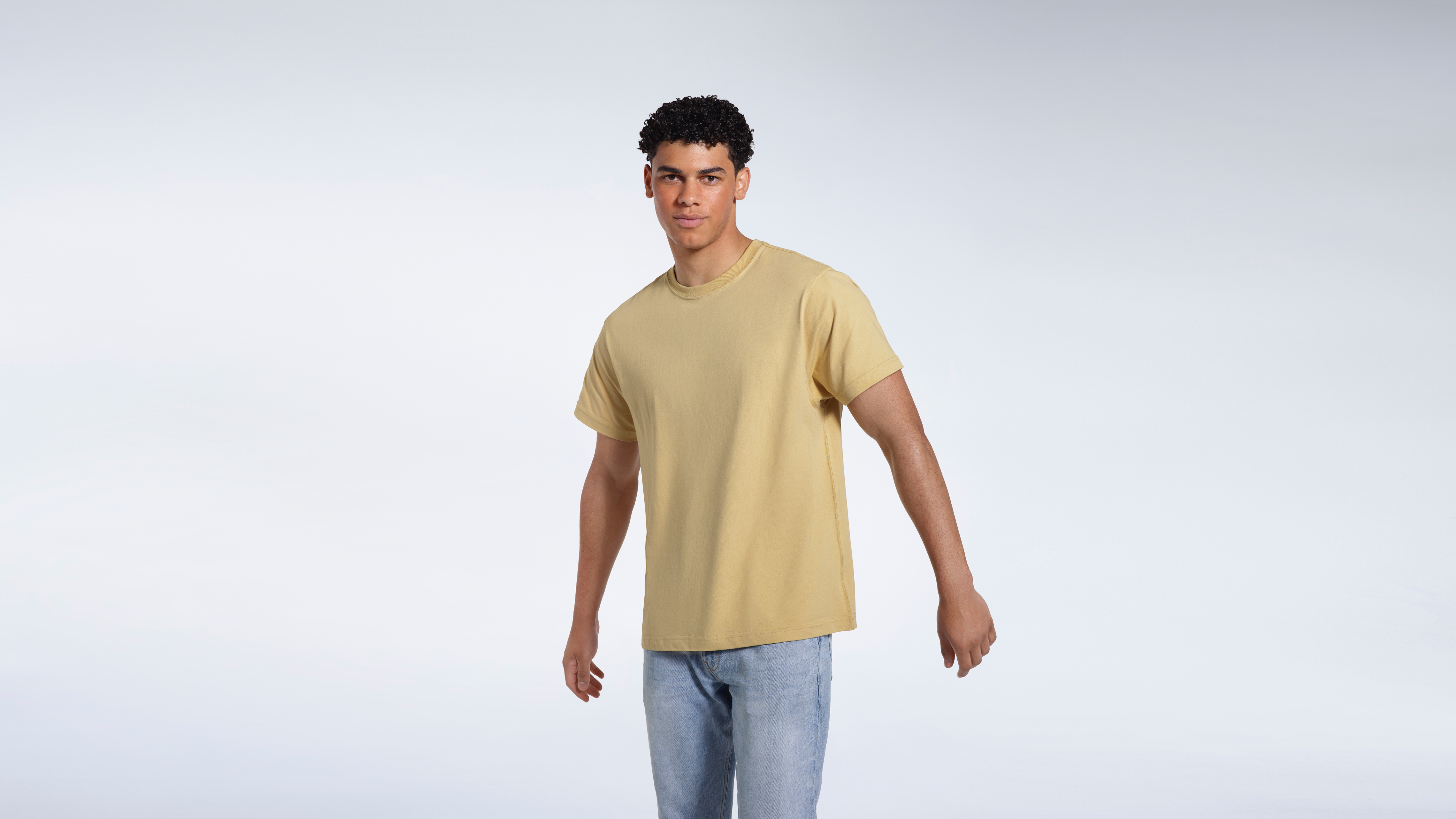 A man looking into the camera, modelling a light khaki organic cotton t shirt.