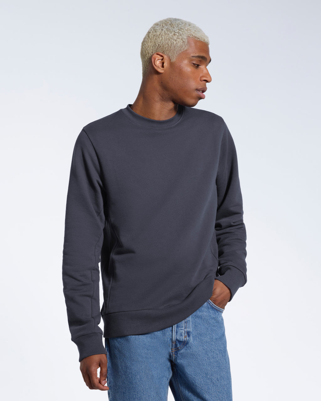 A man looking away from the camera with a hand in his pocket, modelling a plain dark grey french terry organic cotton sweatshirt.