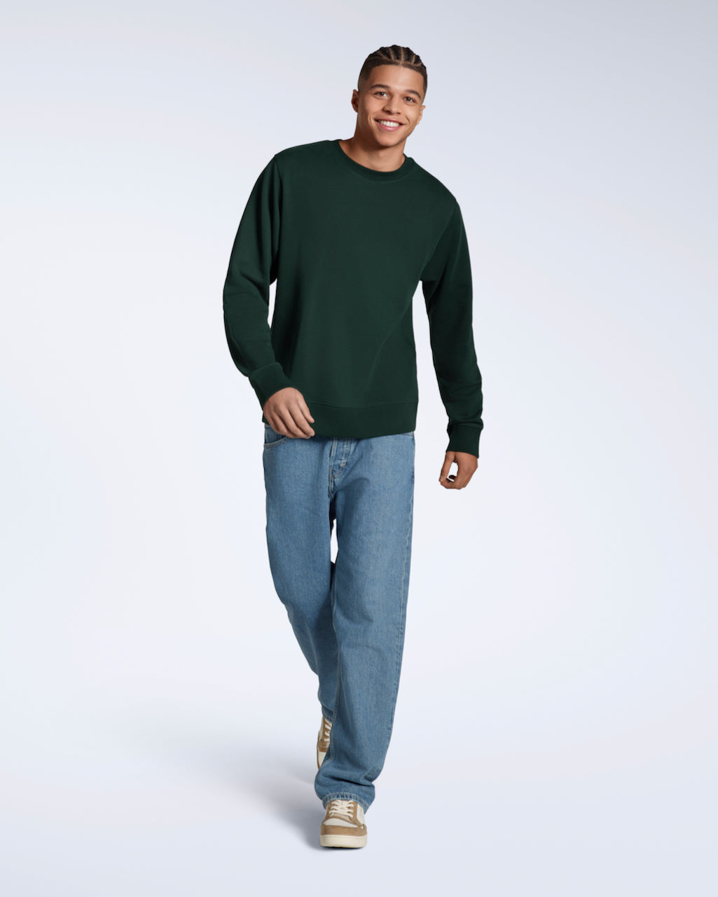 A full body photo of a man walking smiling into the camera, modelling a plain dark green french terry organic cotton sweatshirt.