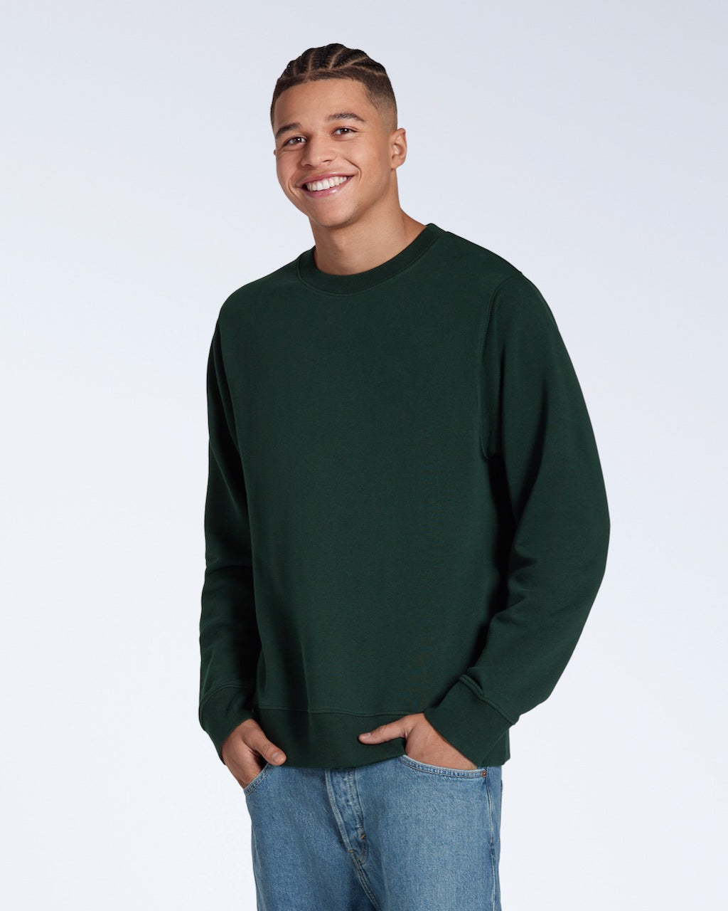 A man smiling into the camera with his hands in his pockets, modelling a plain dark green french terry organic cotton sweatshirt.