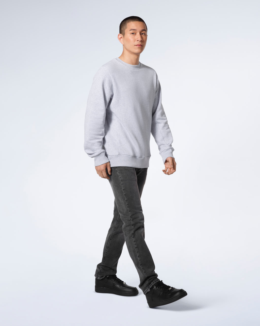 A full body photo of a man walking looking into the camera, modelling a plain grey french terry organic cotton sweatshirt.