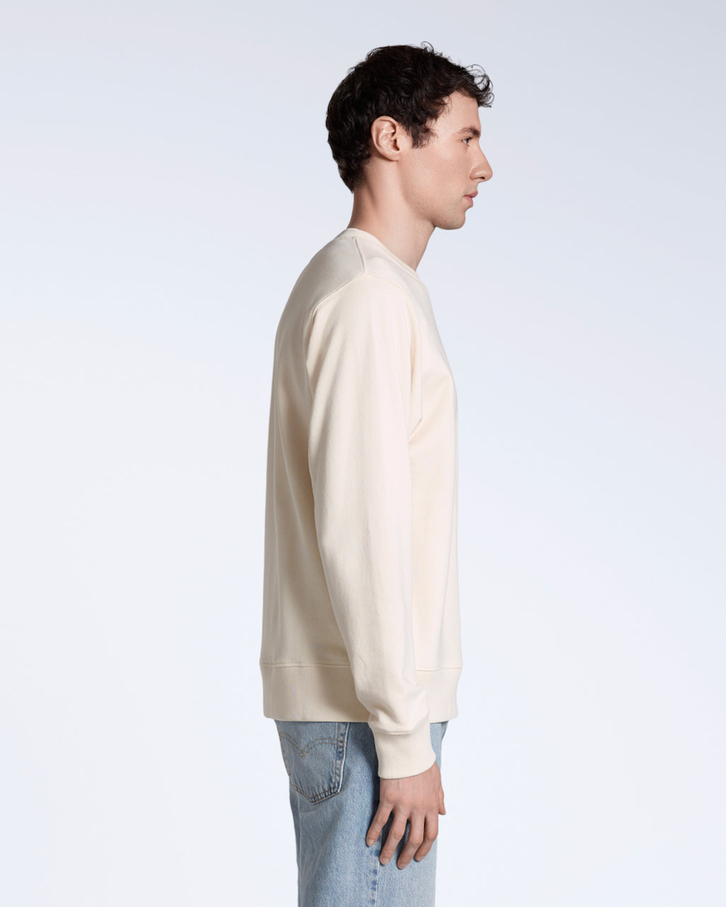 A man facing side on, with his arms by his side, modelling a plain natural coloured, organic cotton sweatshirt.