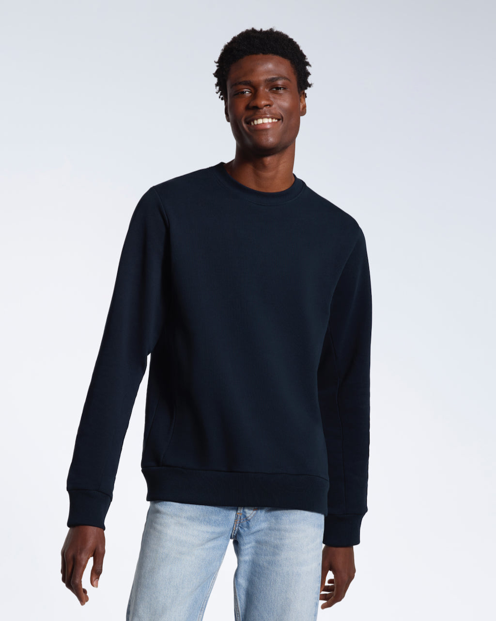 A man looking into the camera smiling with his arms by his side, modelling a plain navy french terry organic cotton sweatshirt.