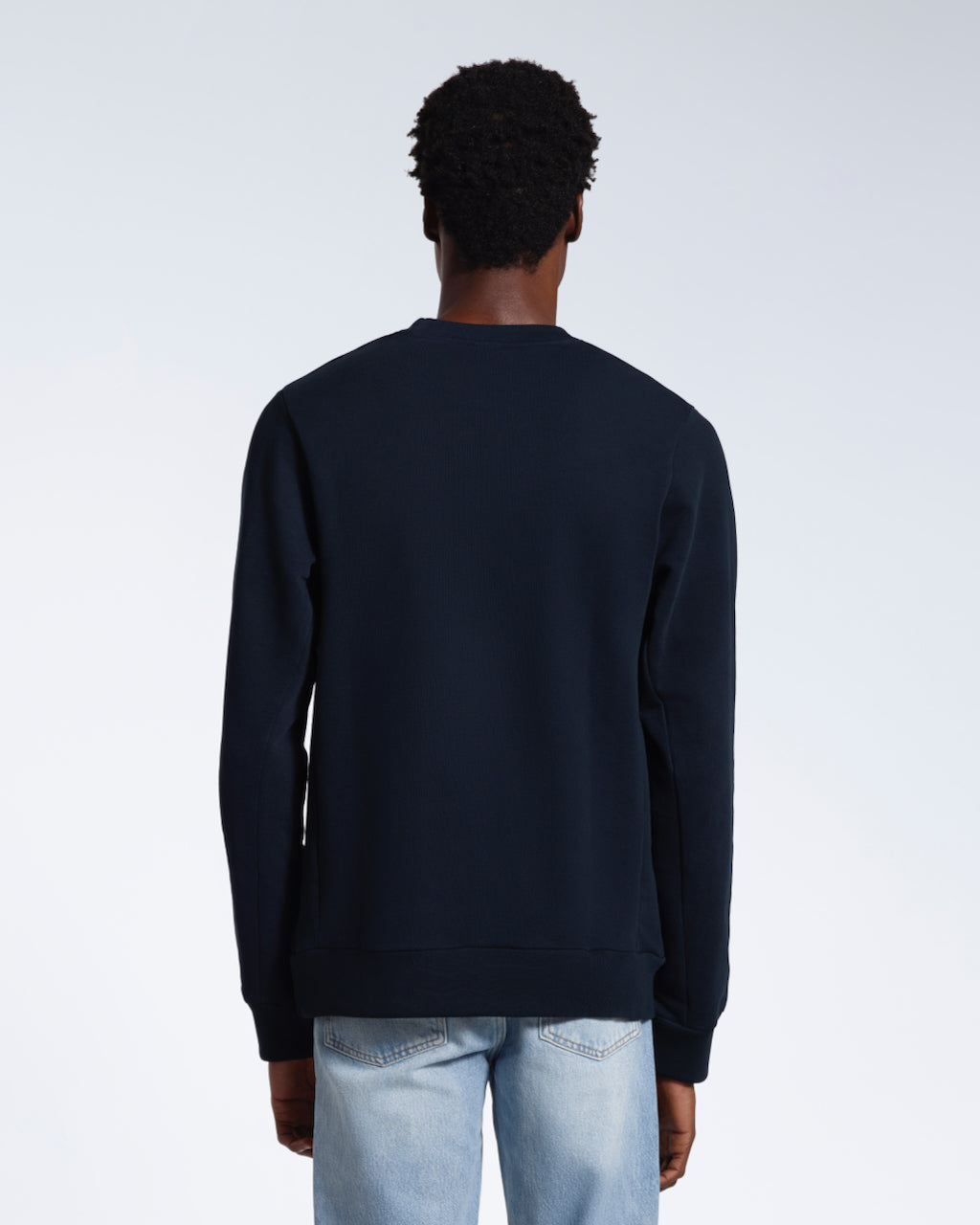 A man facing away from the camera, showing the back of his plain navy french terry organic cotton sweatshirt.