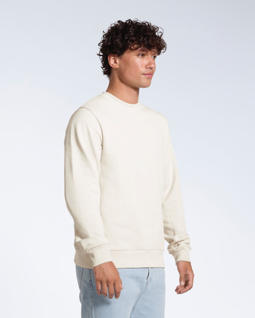 A man looking away from the camera with his arms by his side, modelling a plain off white french terry organic cotton sweatshirt.