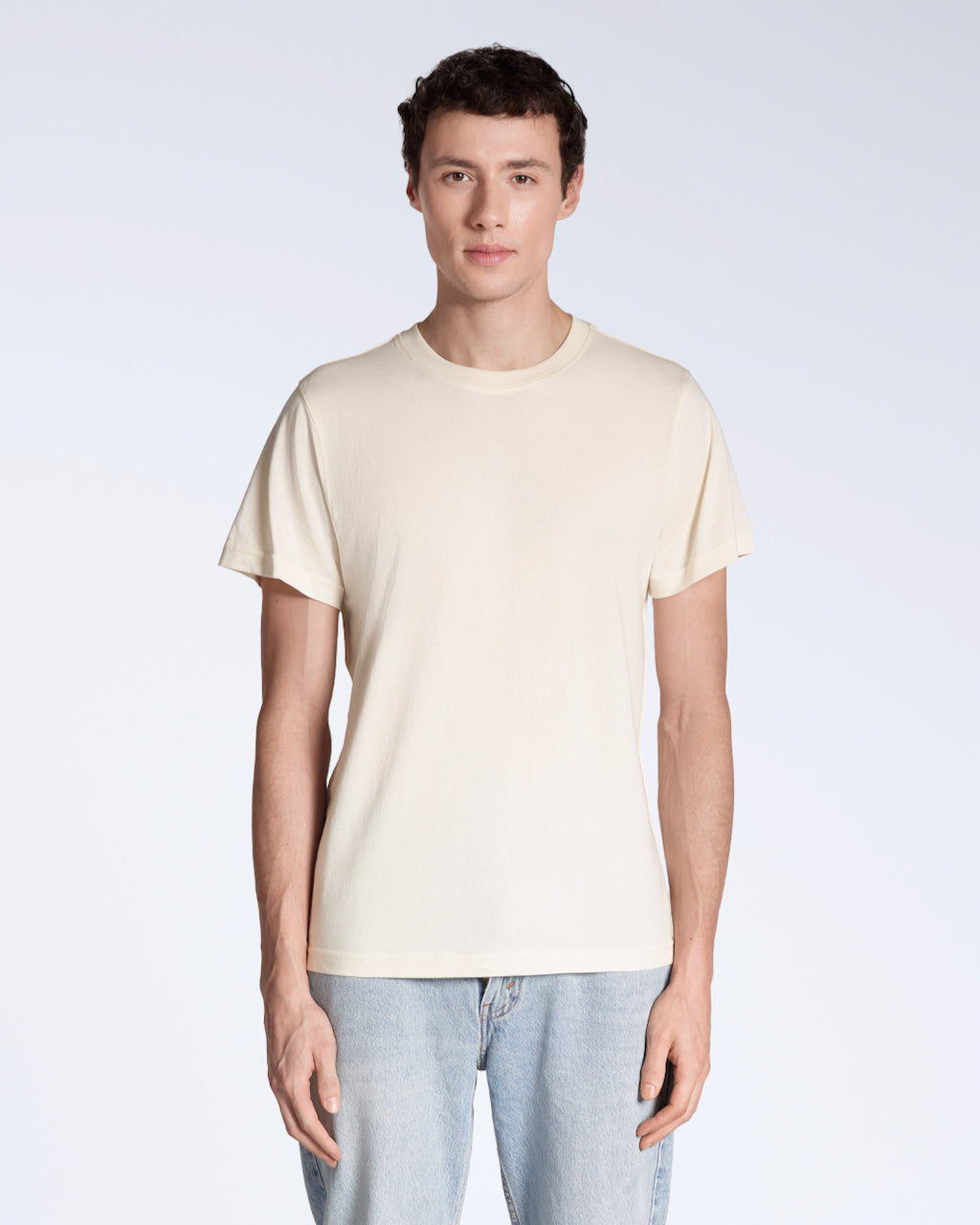 A man facing front on looking into the camera, modelling a plain, natural coloured, organic cotton t shirt.