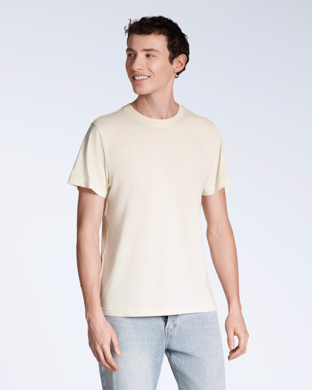 A man smiling, looking away from the camera, modelling a plain natural coloured, organic cotton t shirt.