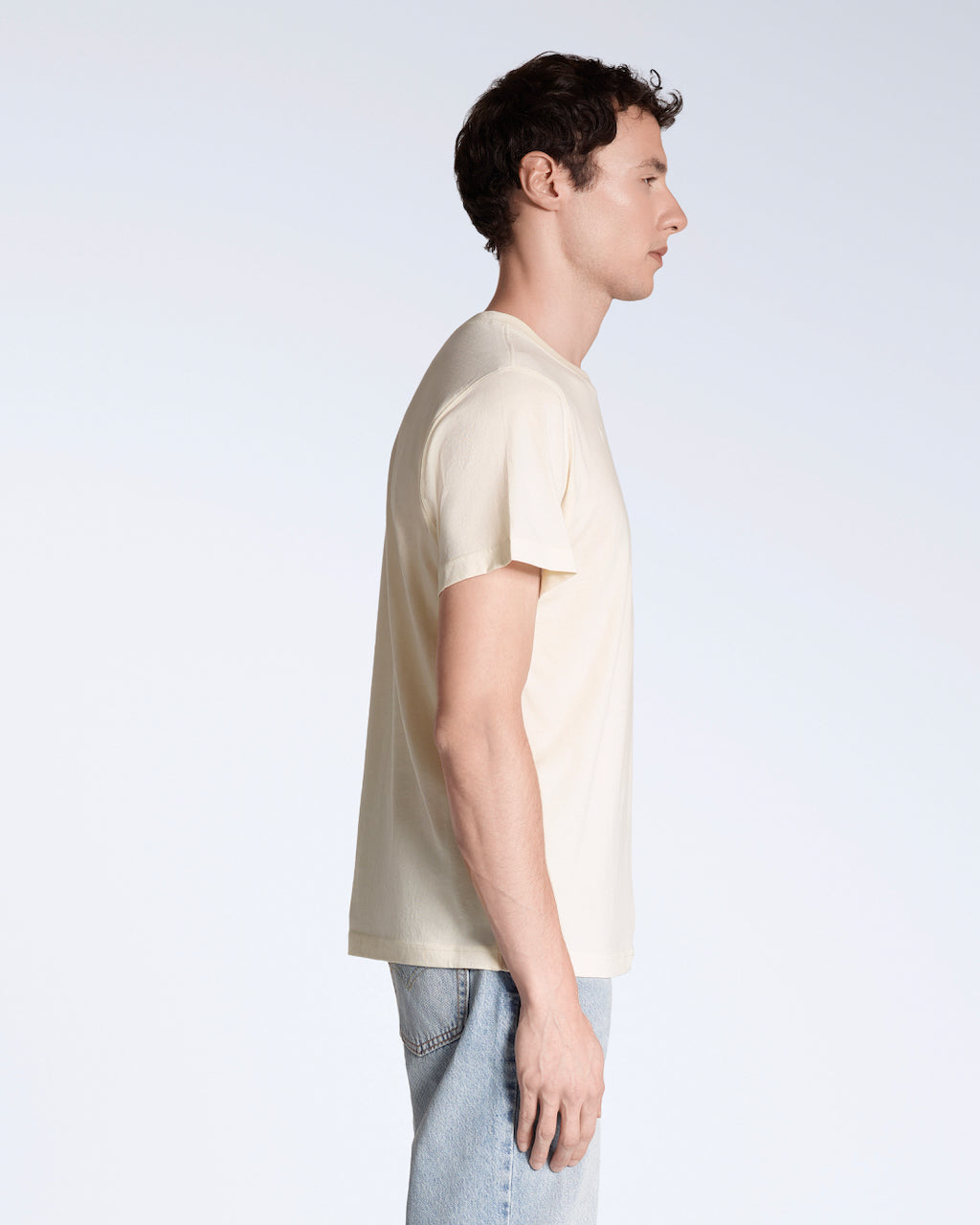 A man facing side on, modelling a plain natural coloured, short sleeve, organic cotton t shirt.