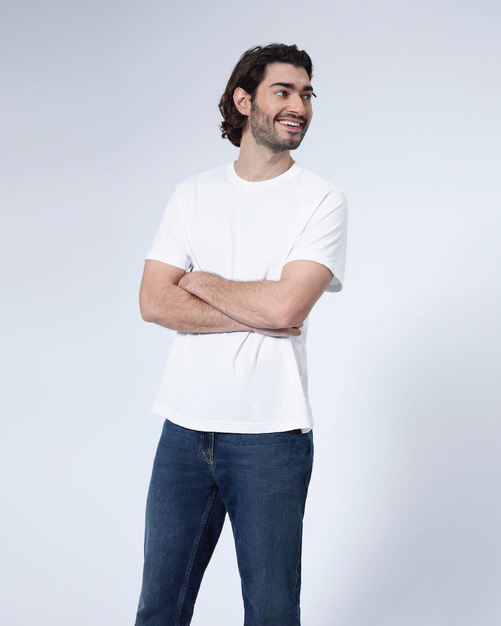 A man looking away from the camera with his arms crossed smiling, modelling a plain white short sleeve organic cotton t shirt.