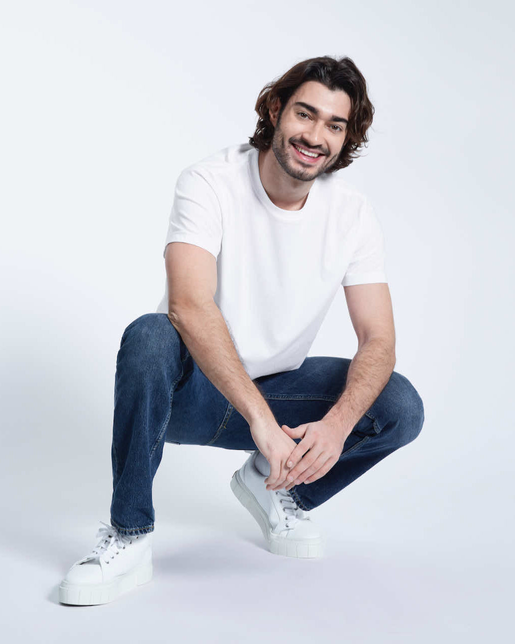 A man crouching down smiling, modelling a plain white short sleeve organic cotton t shirt.