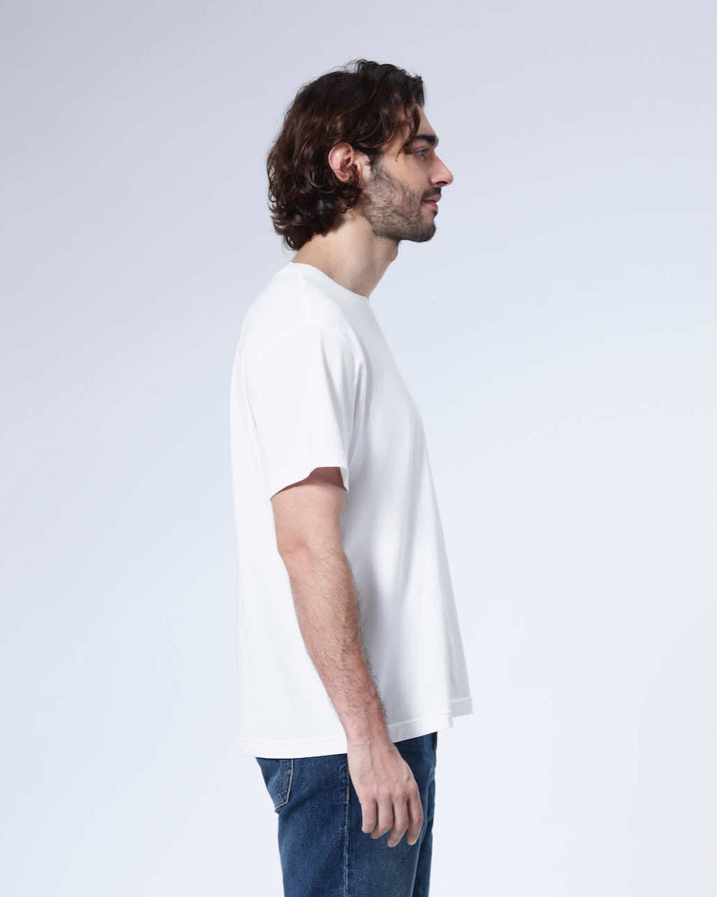 A man facing side on, modelling a plain white short sleeve organic cotton t shirt.