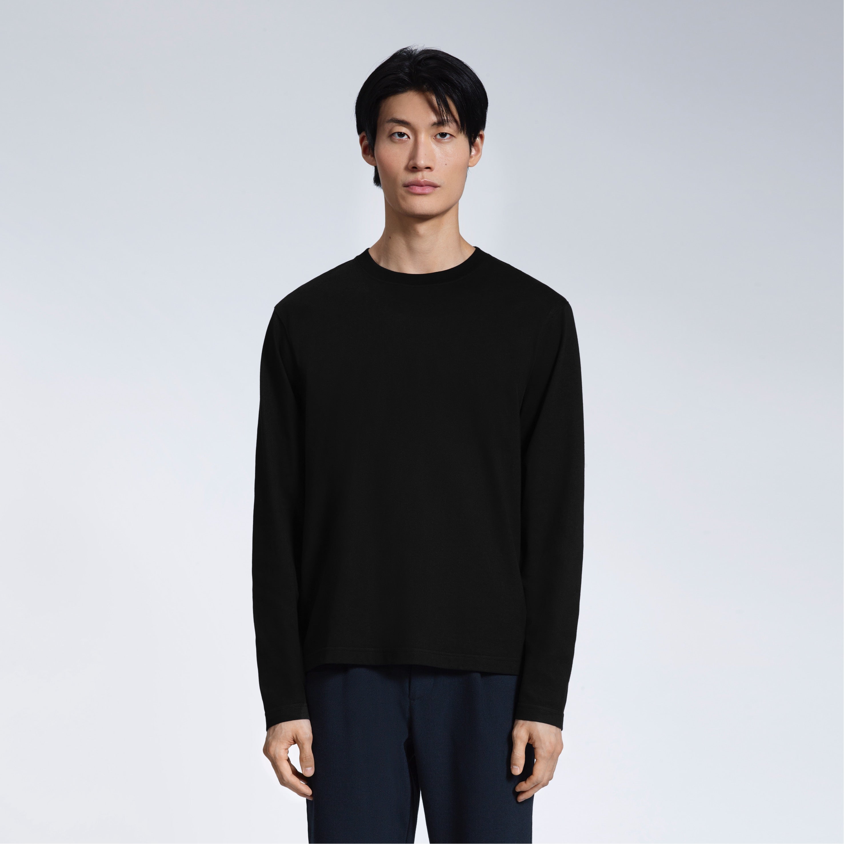 A man standing front on with his arms by his sides, modelling a plain black long sleeve organic cotton t shirt.