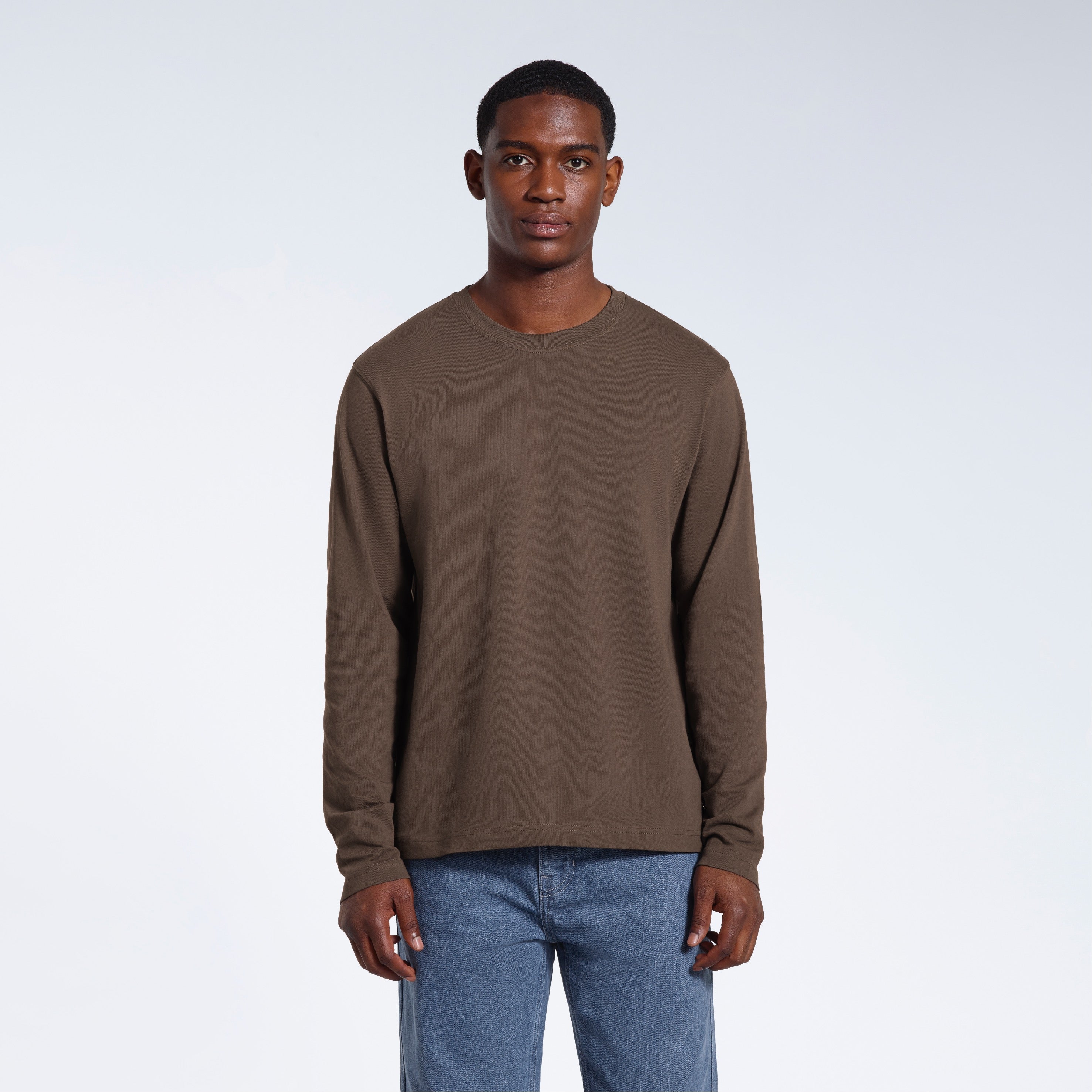 A man standing front on with his arms by his sides, modelling a plain dark khaki long sleeve organic cotton t shirt.