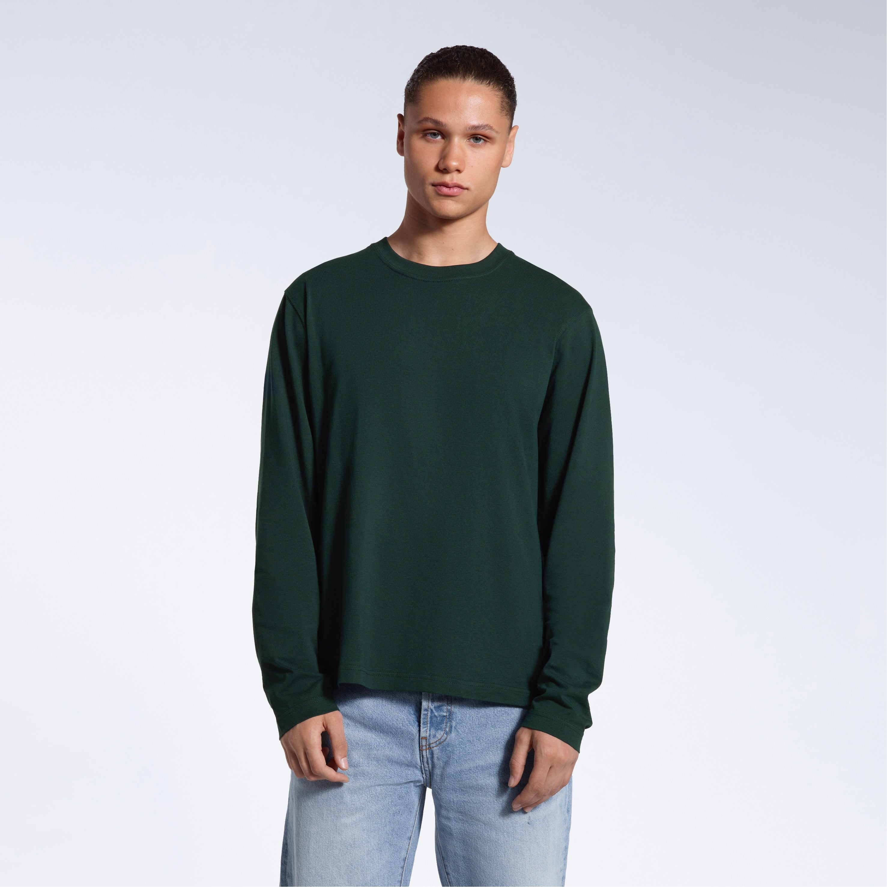 A man standing front on with his arms by his sides, modelling a plain green long sleeve organic cotton t shirt.