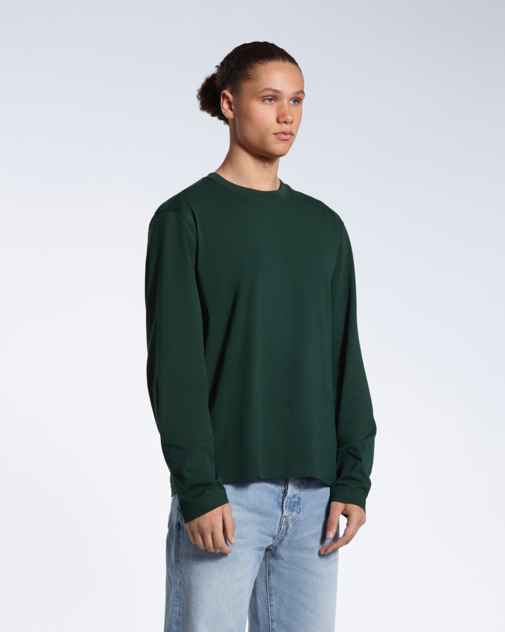 A man looking away from the camera with his arms by his sides, modelling a plain green long sleeve organic cotton t shirt.
