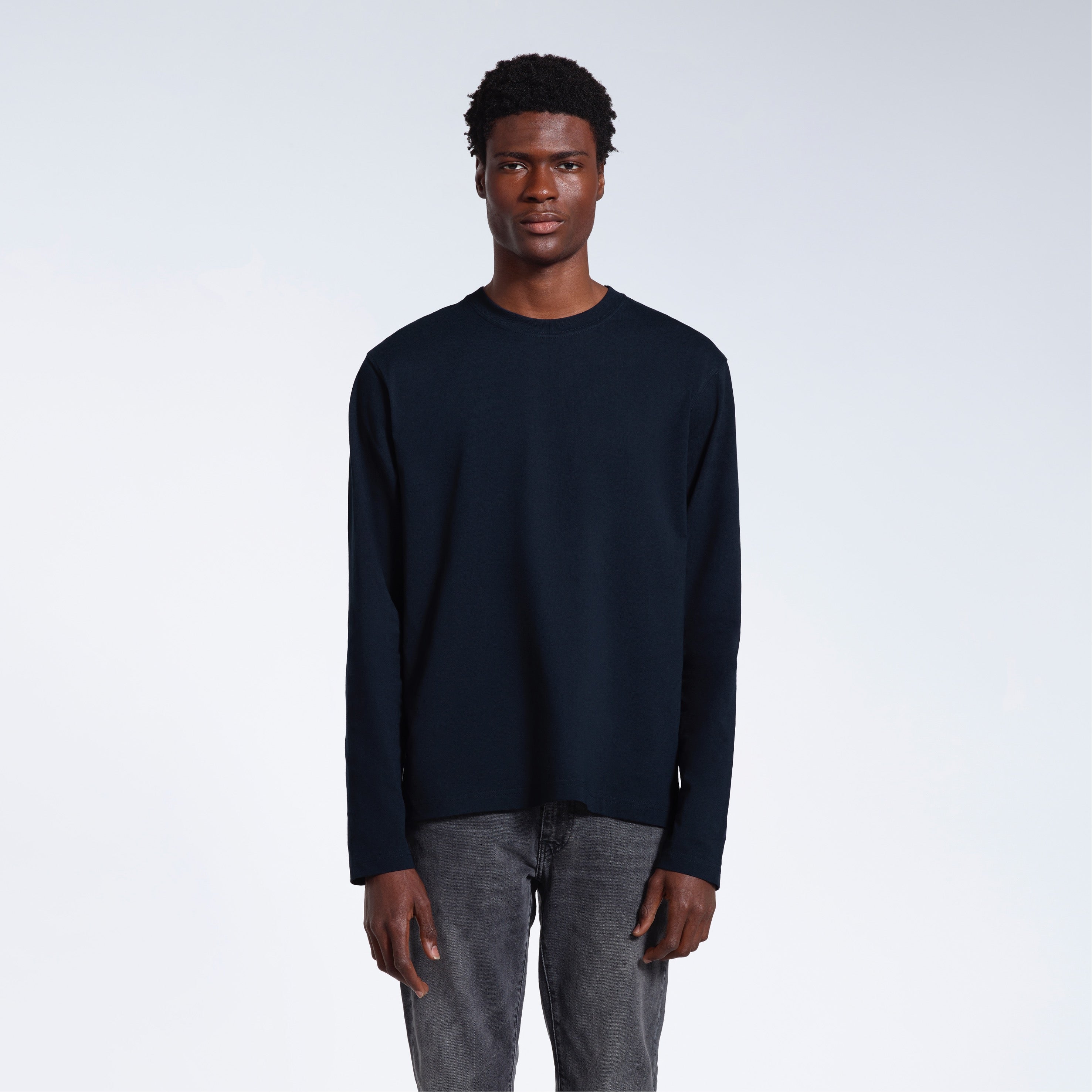 A man standing front on with his arms by his sides, modelling a plain navy long sleeve organic cotton t shirt.