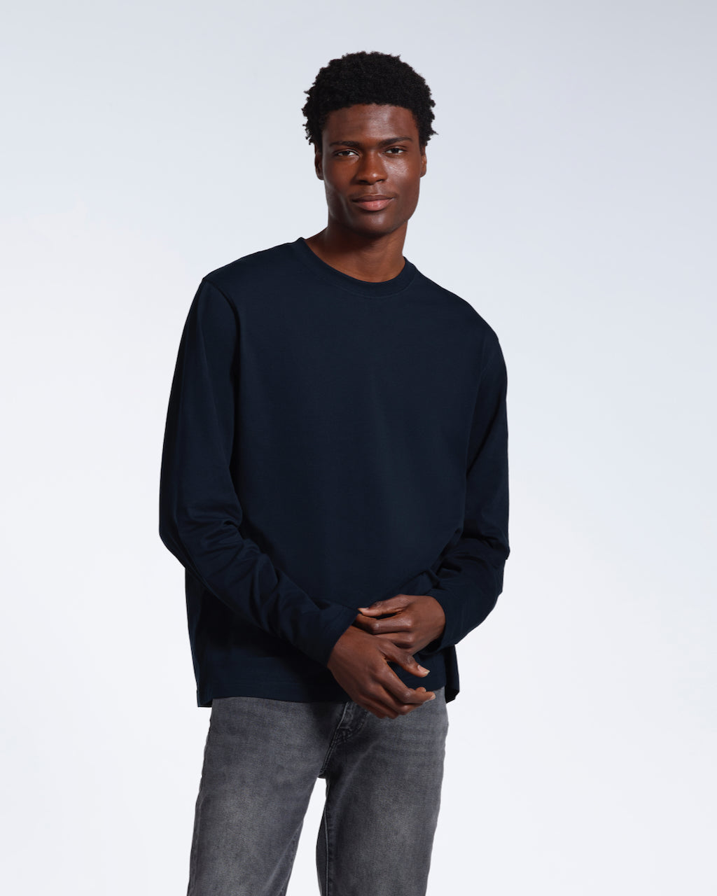 A man looking into the camera, touching the sleeve of his plain navy long sleeve organic cotton t shirt.