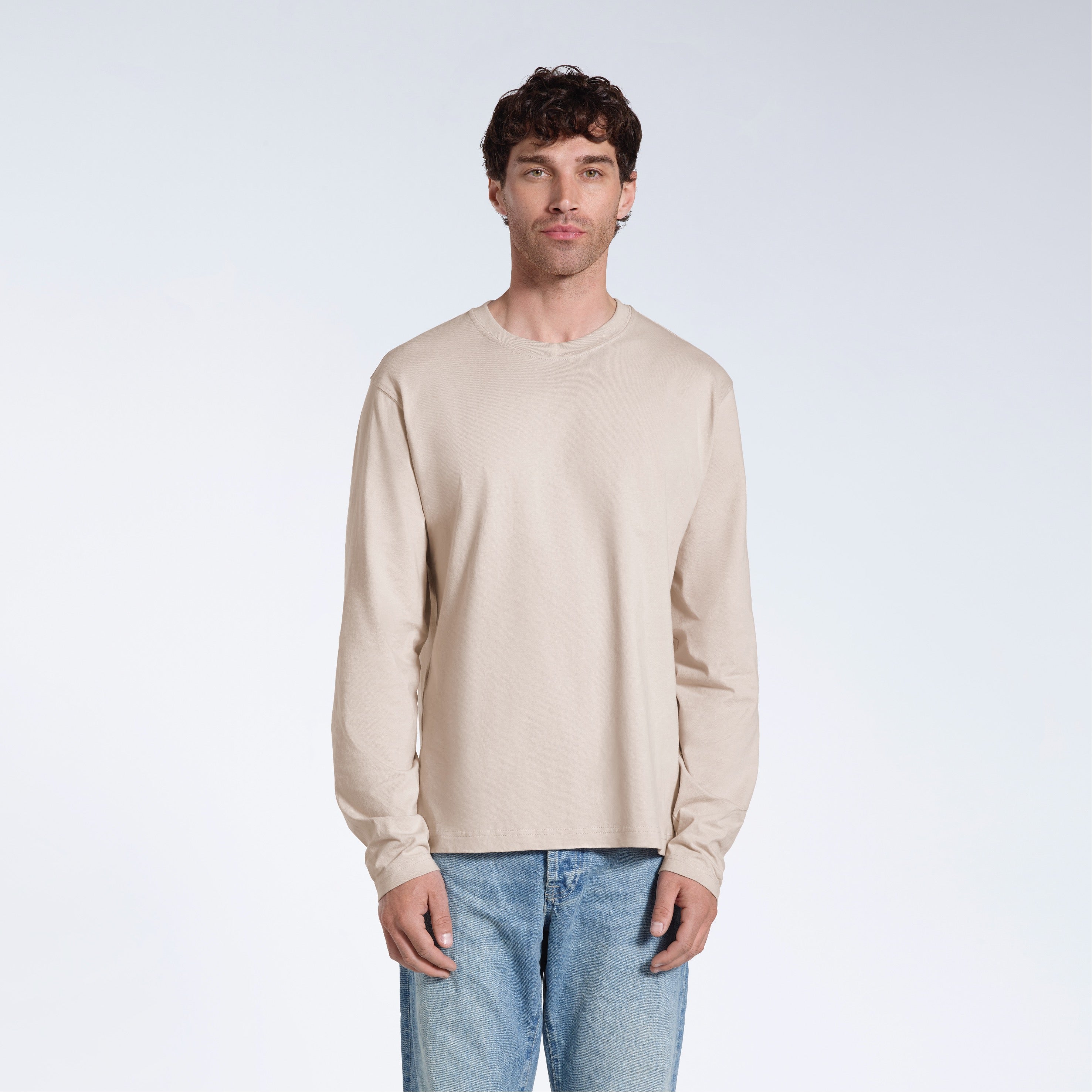 A man standing front on with his arms by his sides, modelling a plain stone long sleeve organic cotton t shirt.
