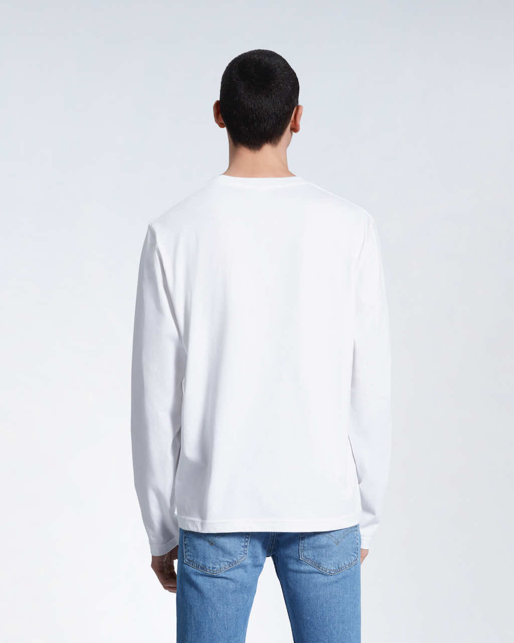 A man standing front on with his arms by his sides, modelling a plain white long sleeve organic cotton t shirt.