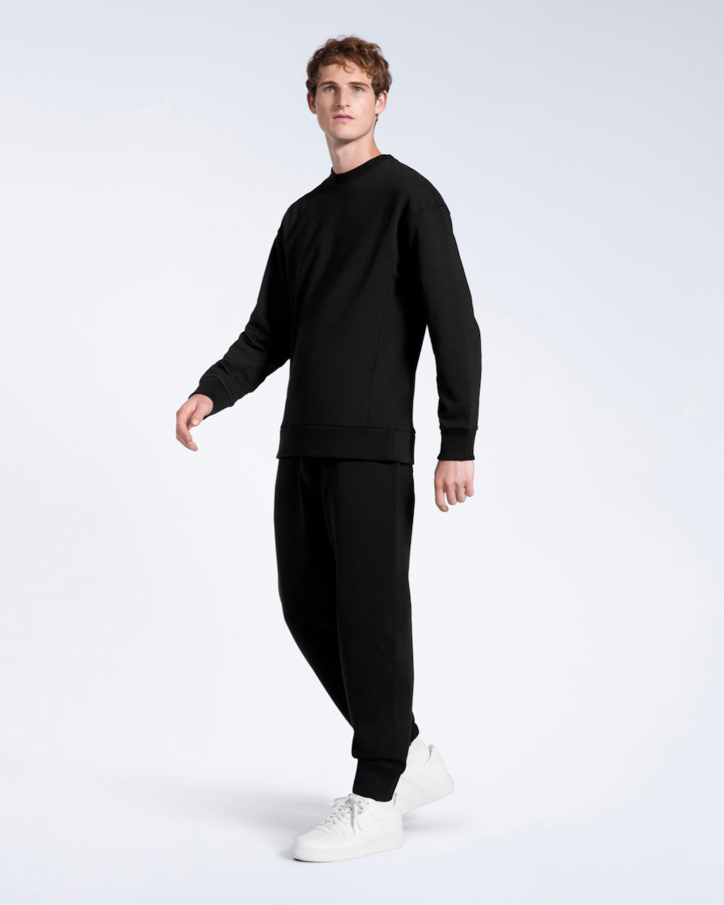 A man looking into the camera, modelling a matching black, organic cotton tracksuit set.
