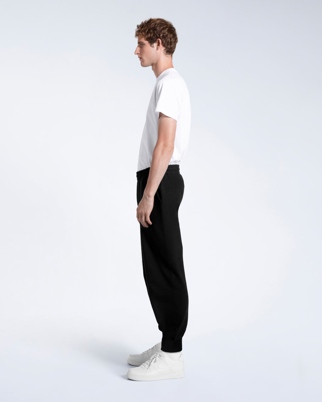 A man facing side on with his arms by his sides, modelling a pair of black organic cotton joggers.