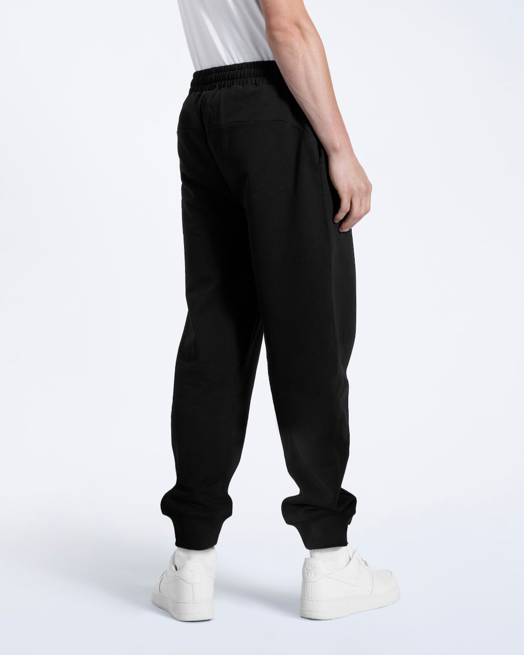 A man facing away from the camera looking back, modelling a pair of black organic cotton joggers.