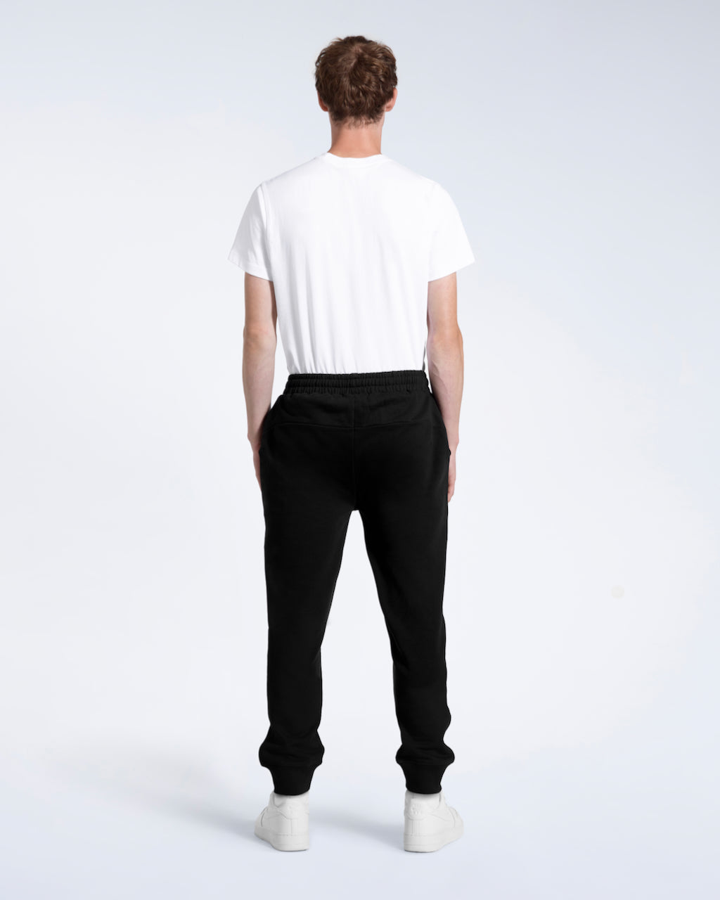 A man with his back to the camera with his arms by his sides, modelling a pair of black organic cotton joggers.