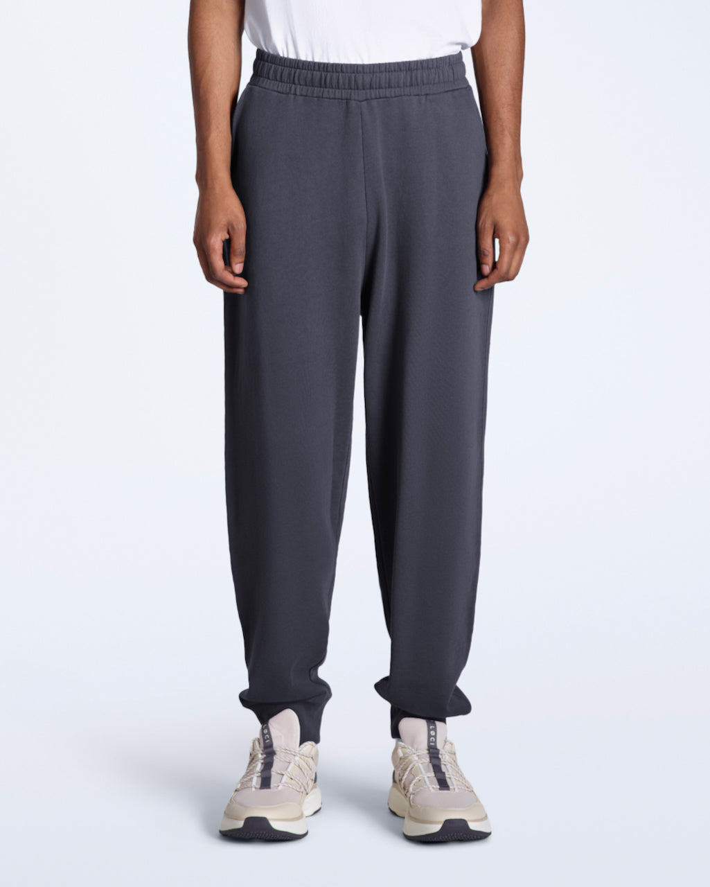 A person with their arms by their sides, modelling a pair of men's dark grey organic cotton joggers.