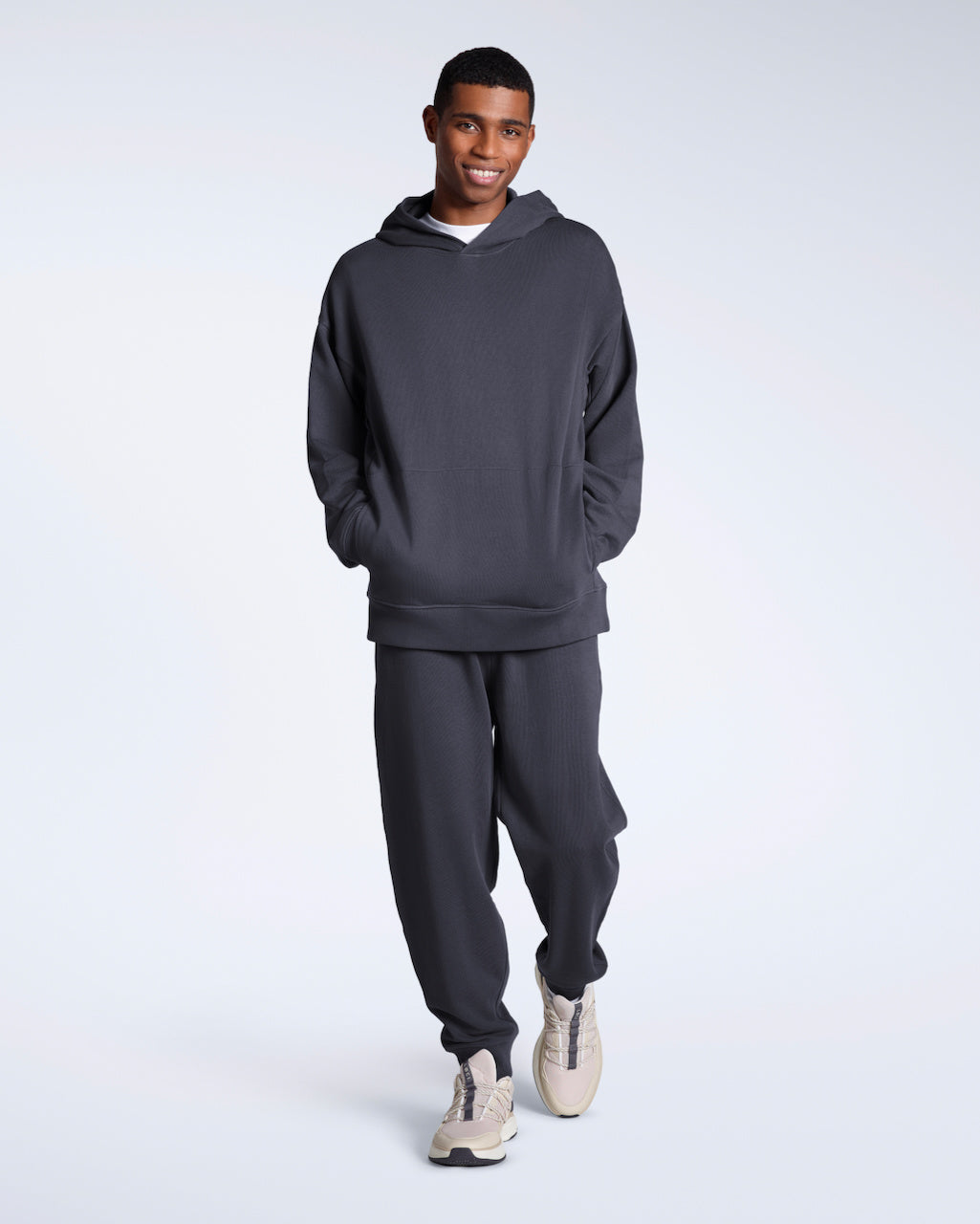A man looking down and touching his t shirt, modelling a pair of dark grey organic cotton joggers.