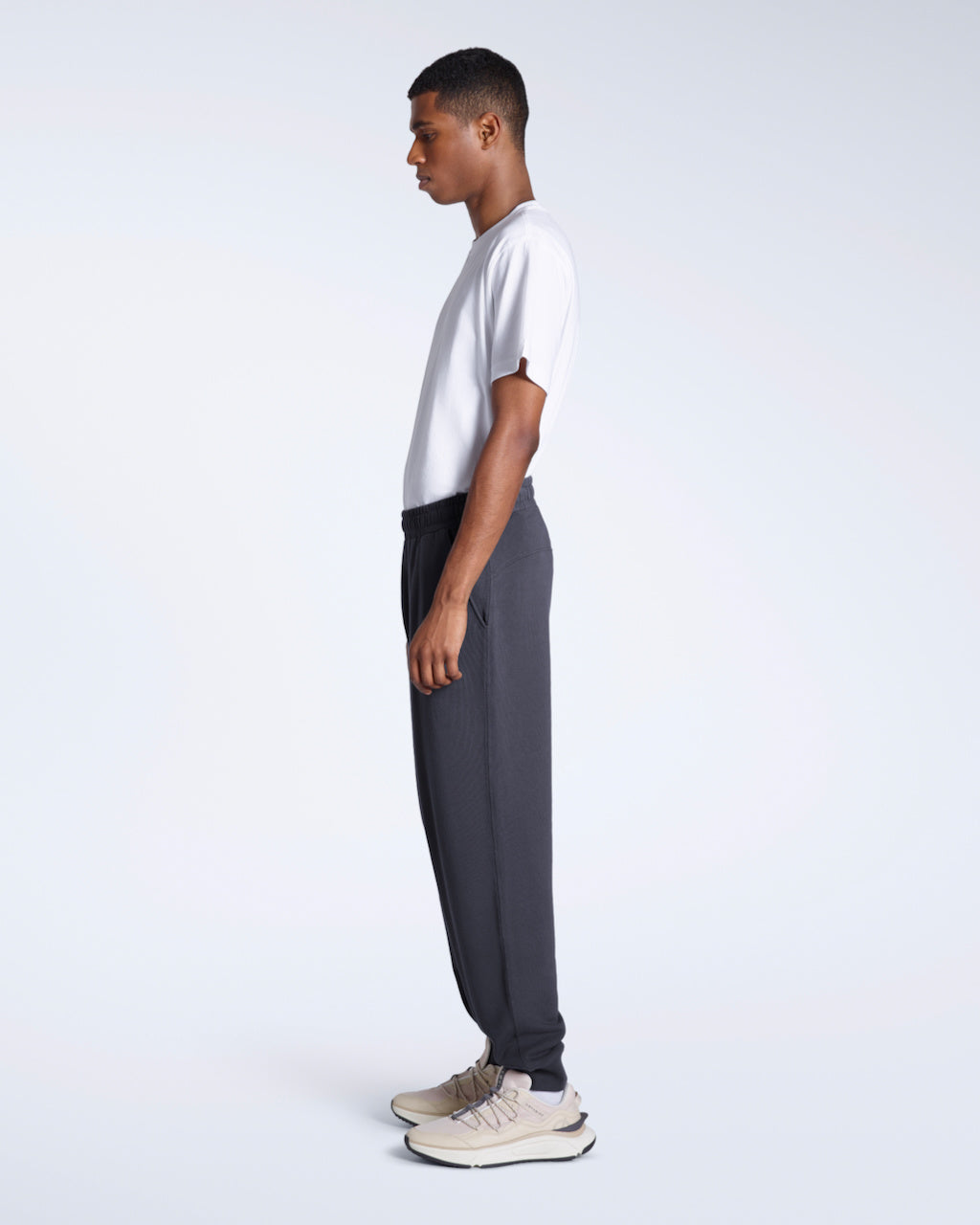 A man facing side on with his arms by his sides, modelling a pair of dark grey organic cotton joggers.