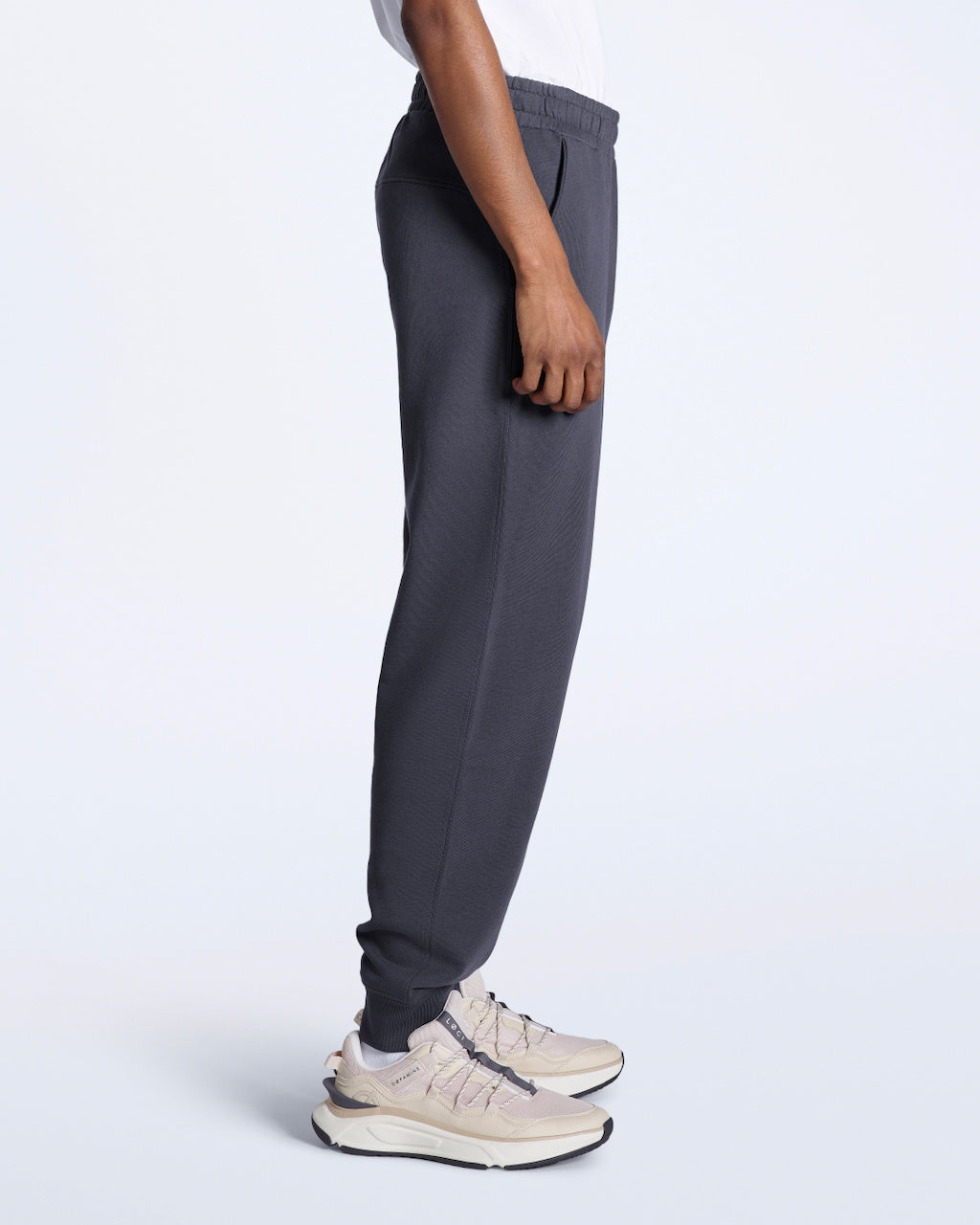 A man facing side on with his arms by his sides, modelling a pair of dark grey organic cotton joggers.