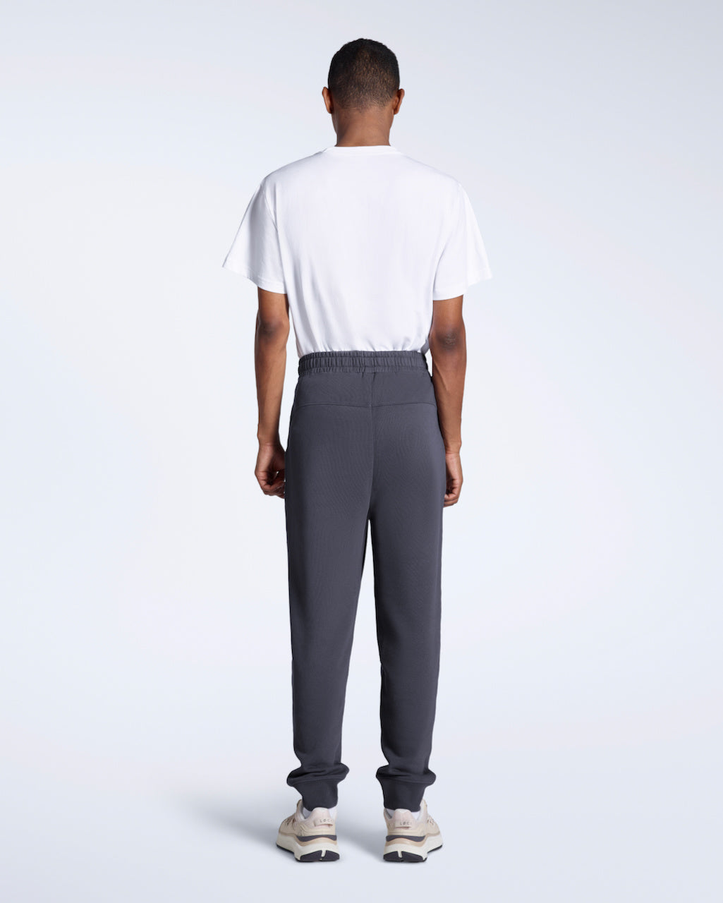 A man with his back to the camera with his arms by his sides, modelling a pair of dark grey organic cotton joggers.