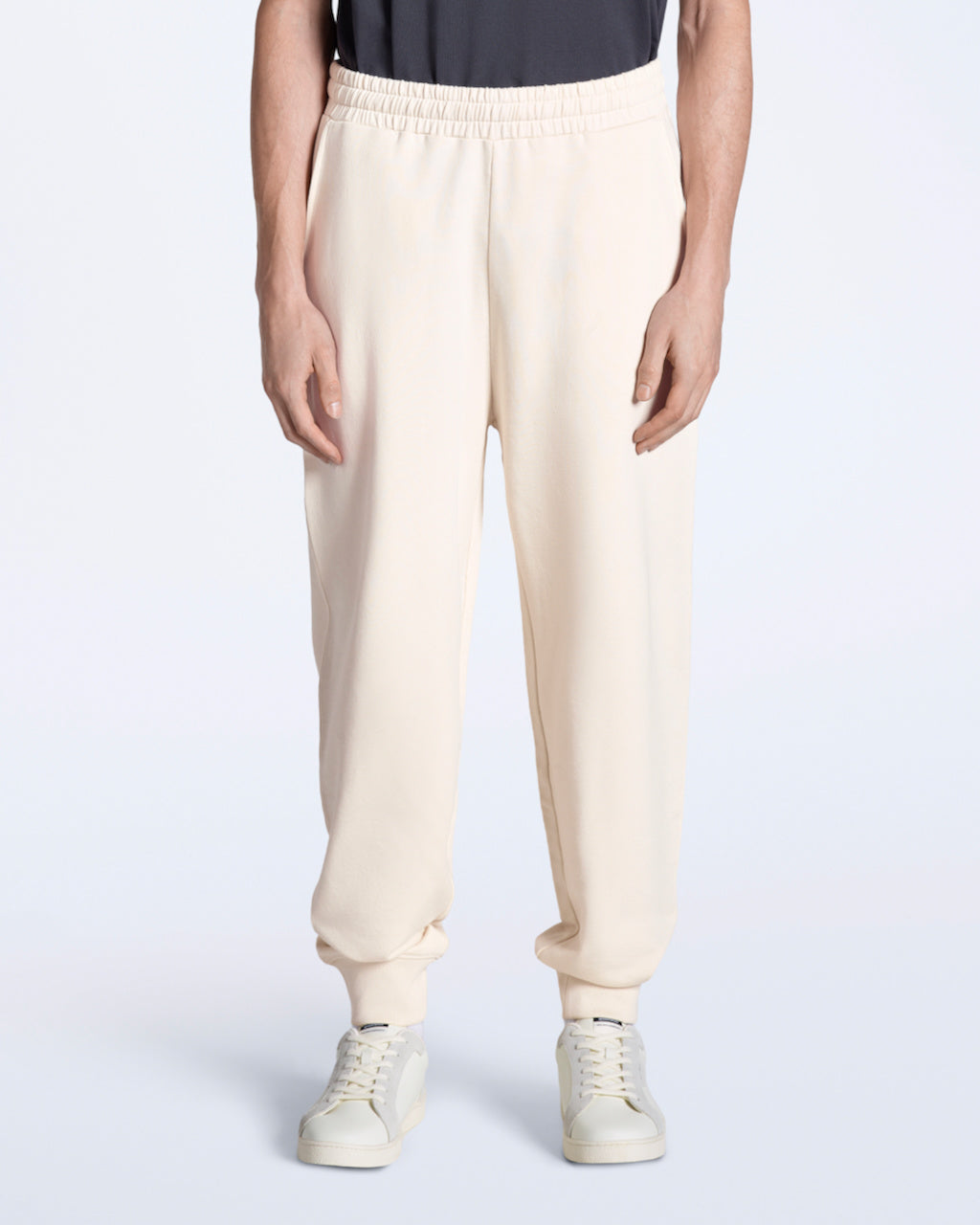 A person with their arms by their sides, modelling a pair of men's natural coloured organic cotton joggers.