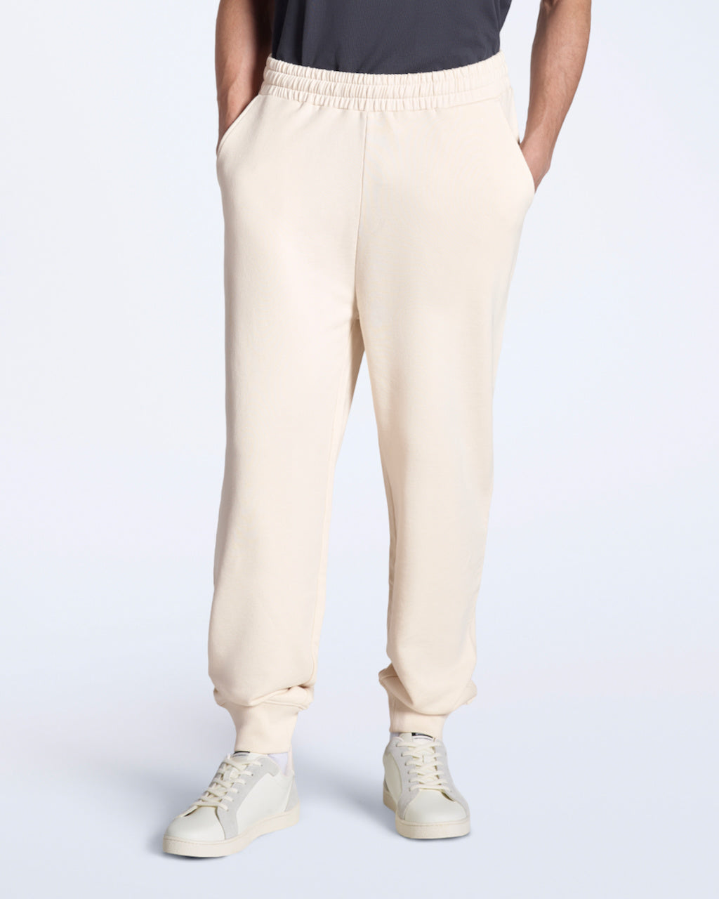 A person with their hands in their pockets, modelling a pair of natural coloured organic cotton joggers.