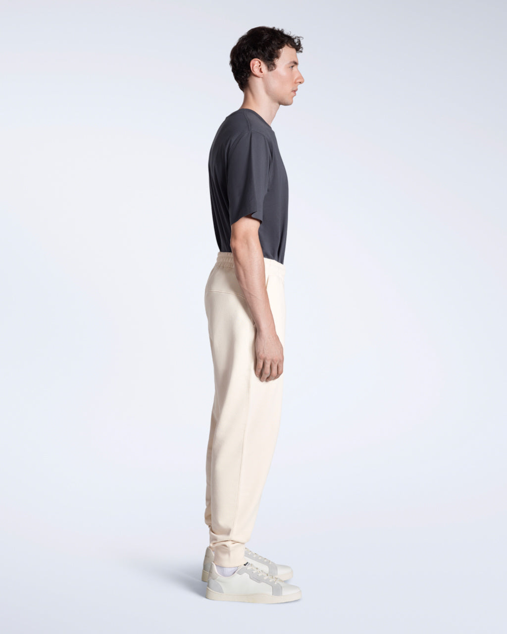 A man facing side on with his arms by his sides, modelling a pair of natural coloured organic cotton joggers.