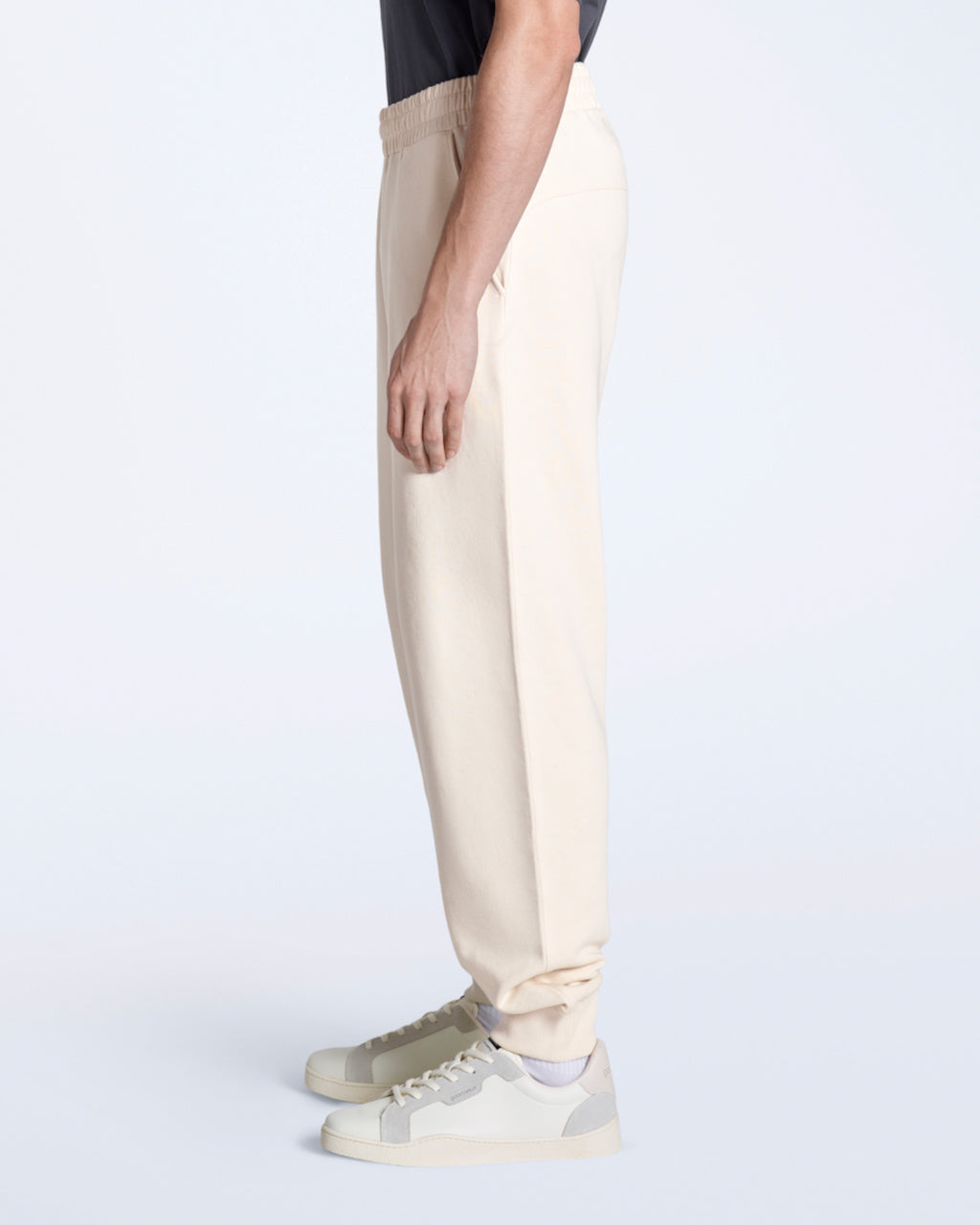 A man facing side on with his arms by his sides, modelling a pair of natural coloured organic cotton joggers.