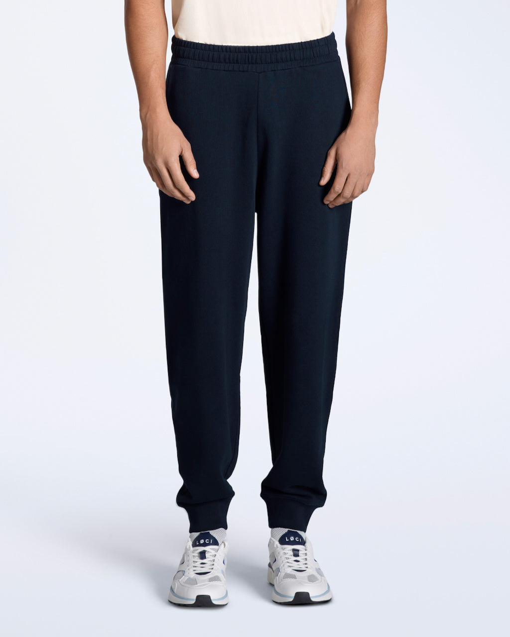 A person with their arms by their sides, modelling a pair of men's navy organic cotton joggers.
