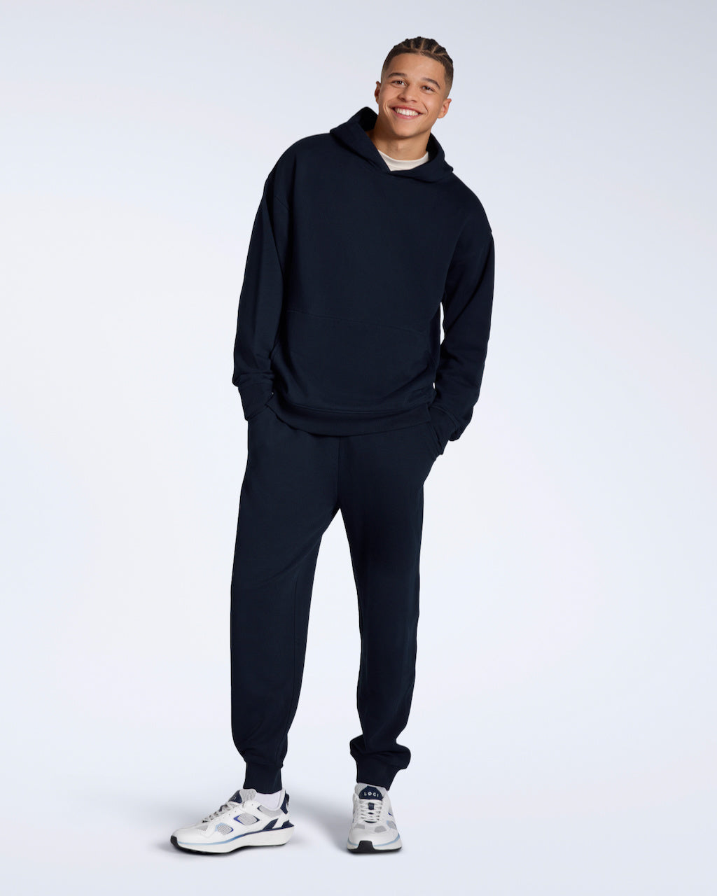 A man smiling into the camera with his arms folded, modelling a pair of navy organic cotton joggers.