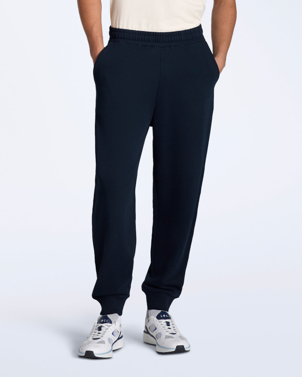 A person with their hands in their pockets, modelling a pair of navy organic cotton joggers.